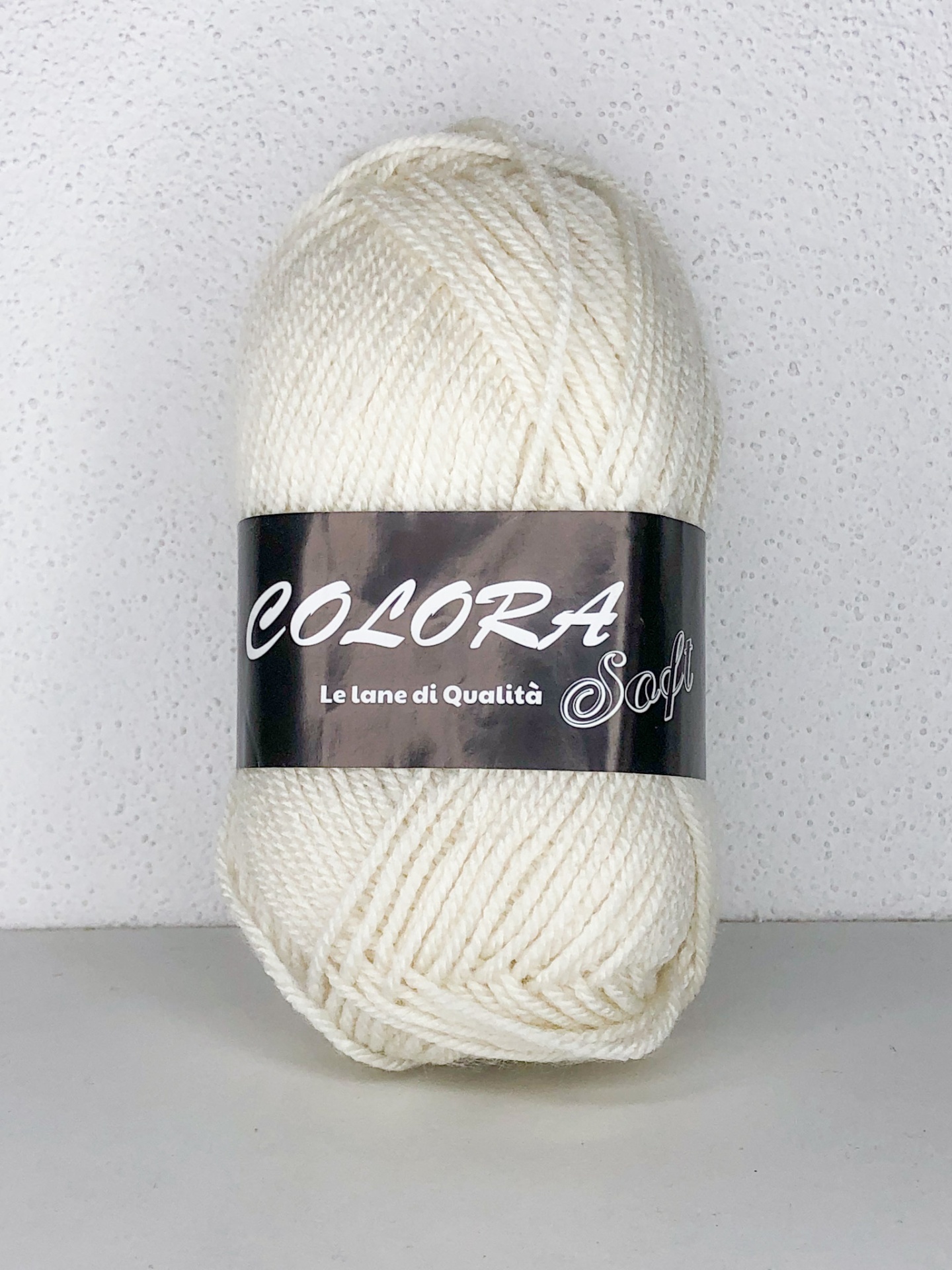 Novelo de lã branca com etiqueta preta e texto, em fundo branco texturado