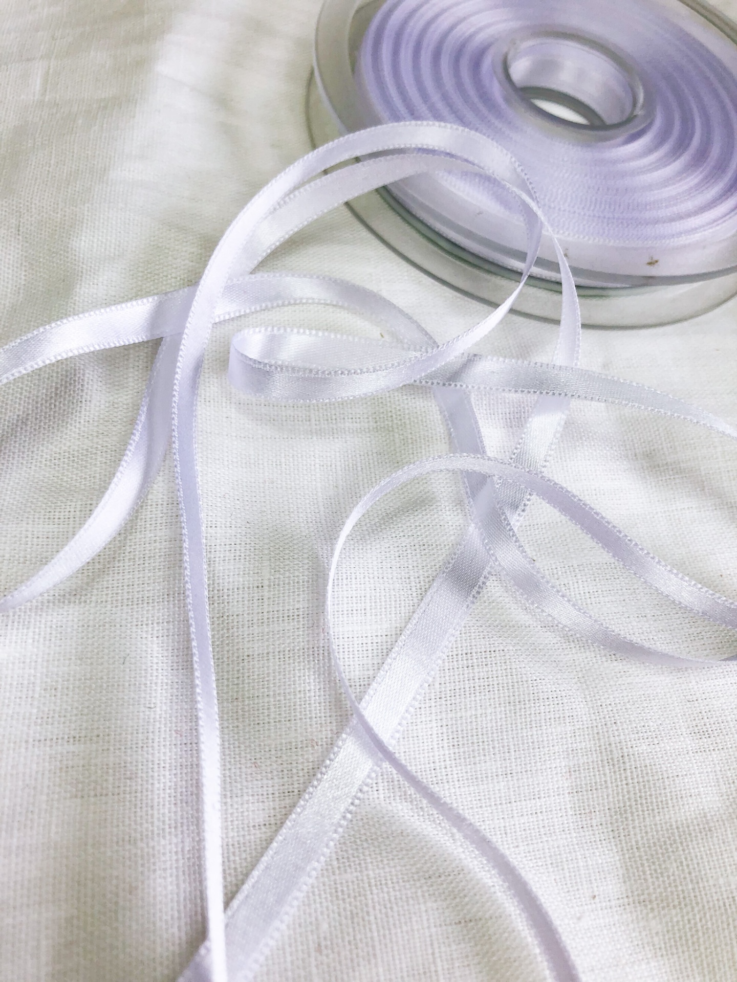 Rolo de fita branca de cetim com fita desenrolada sobre tecido branco