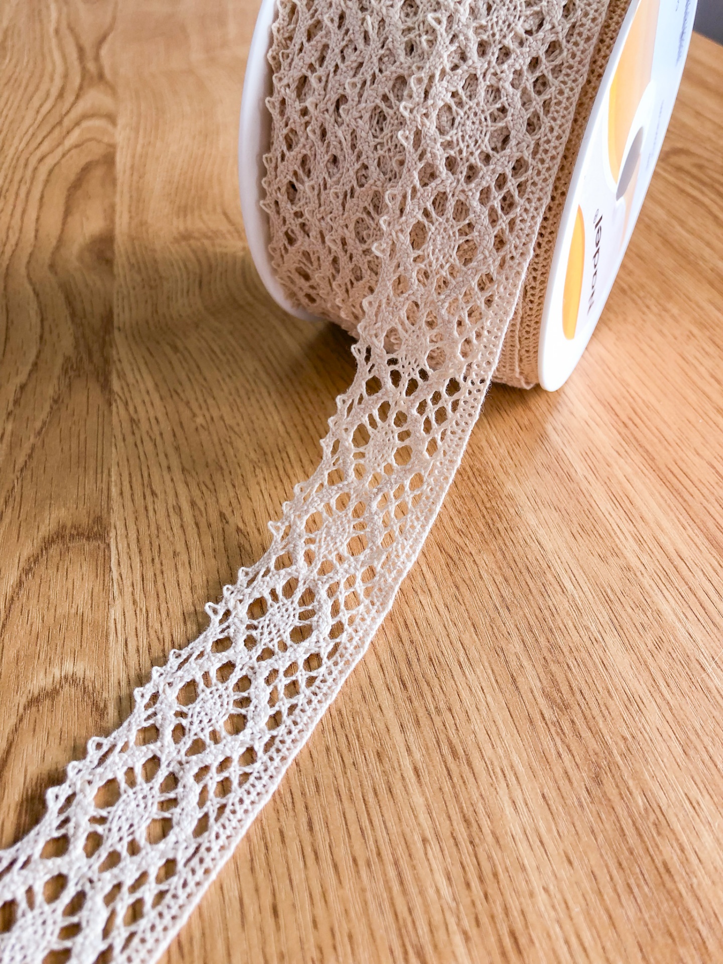 Rolo de fita rendada bege clara com padrão floral sobre madeira clara