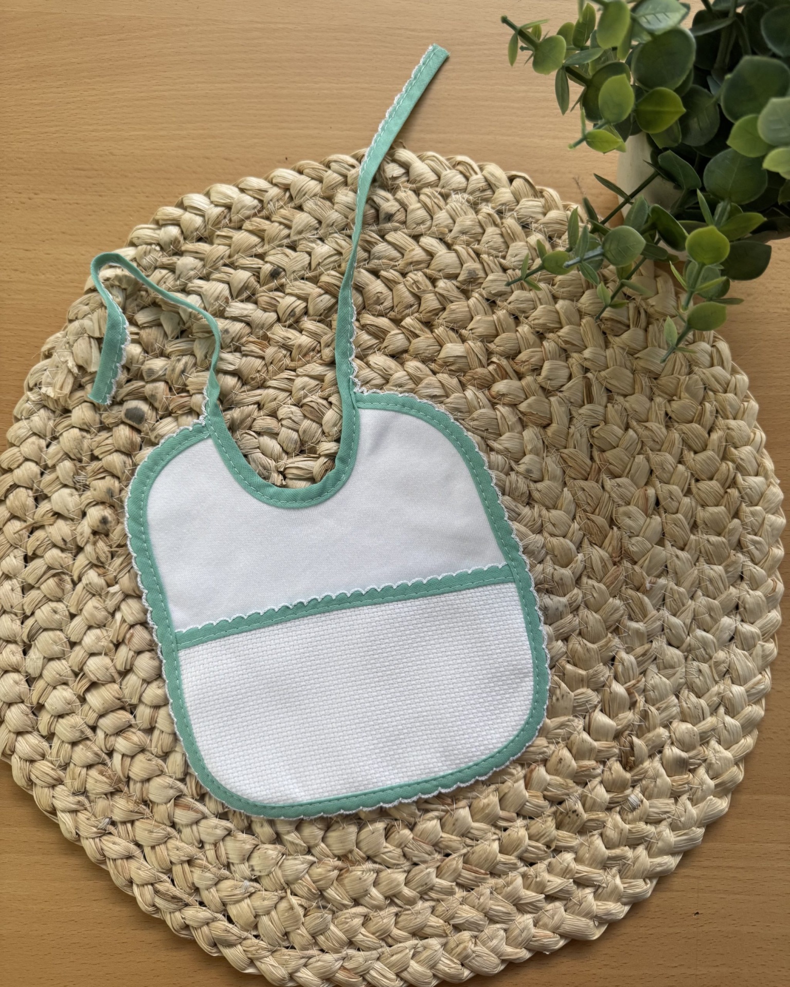 Babete branco com bordas verde-água sobre tapete de fibras naturais e planta verde