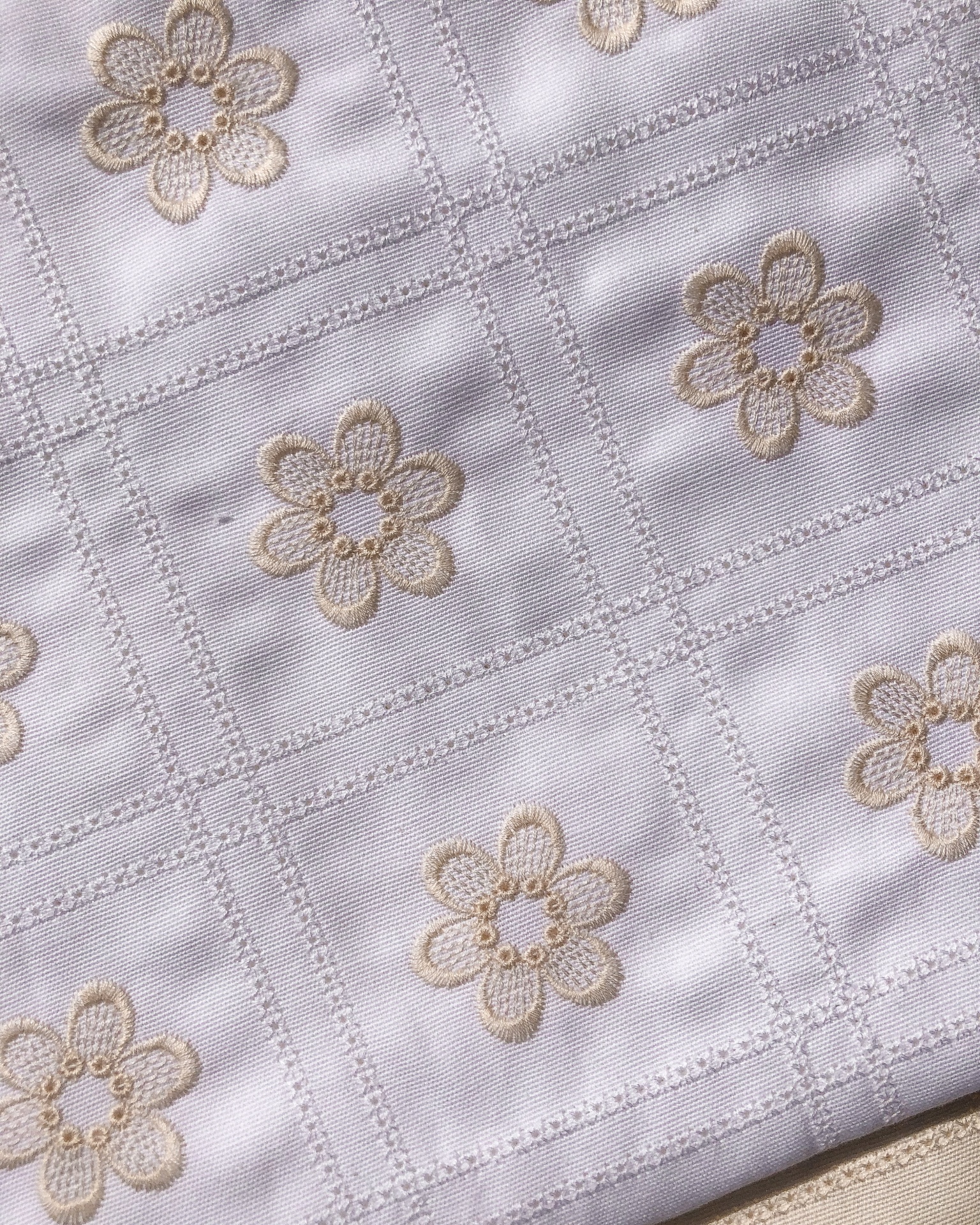 Tecido branco bordado com flores bege em padrão quadrado