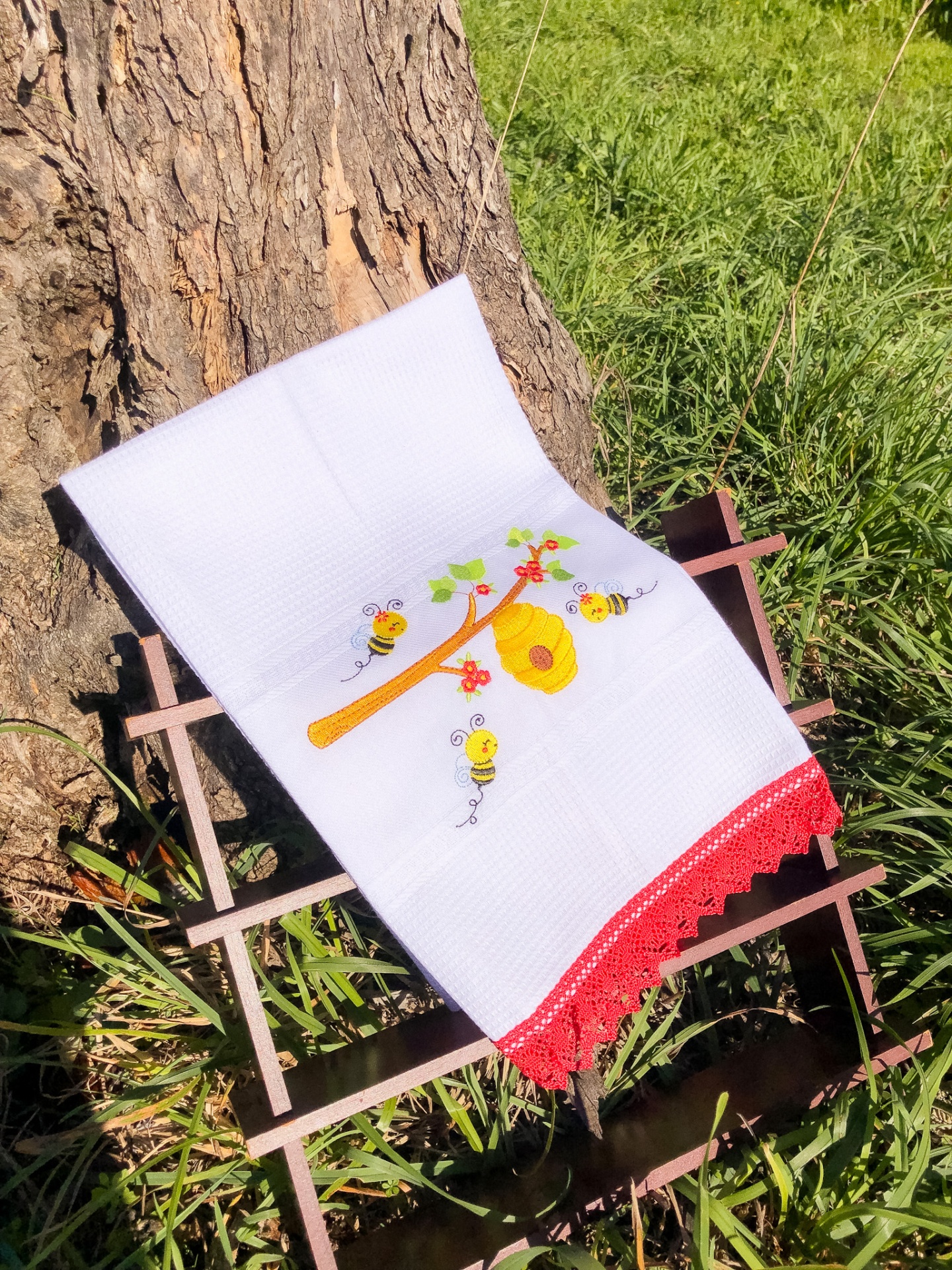 Toalha bordada branca com padrão de abelhas e renda vermelha ao ar livre