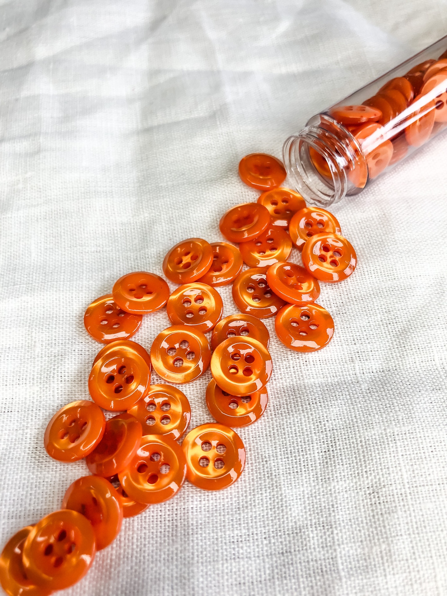 Botões laranja translúcidos com quatro furos num tecido branco