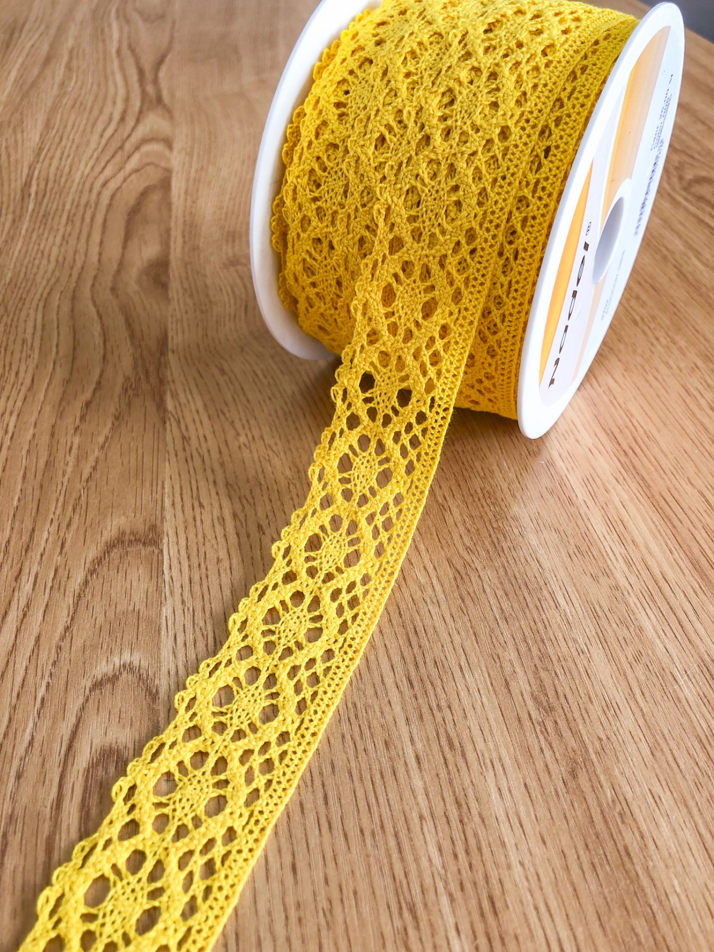 Rolo de renda amarela com padrão floral sobre mesa de madeira