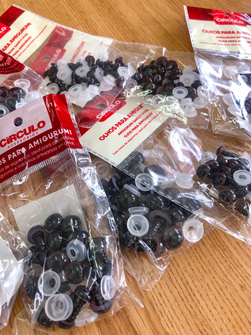 Pacotes com olhos de segurança para amigurumi da marca Círculo sobre mesa de madeira.