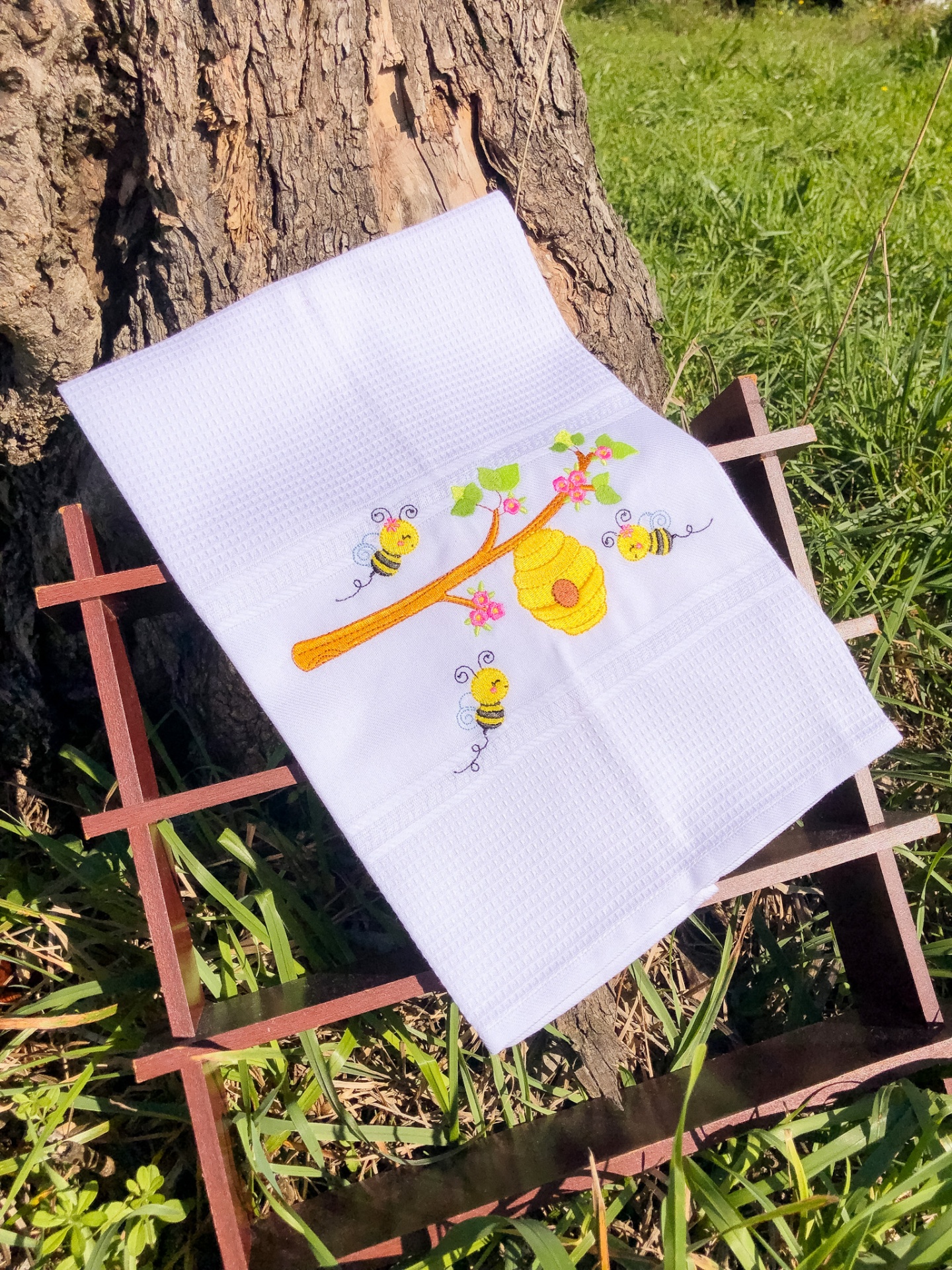 Pano de prato branco com bordado de abelhas e favo de mel ao ar livre