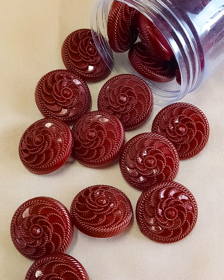 Botões vermelhos brilhantes com padrão em espiral em frasco e sobre tecido branco