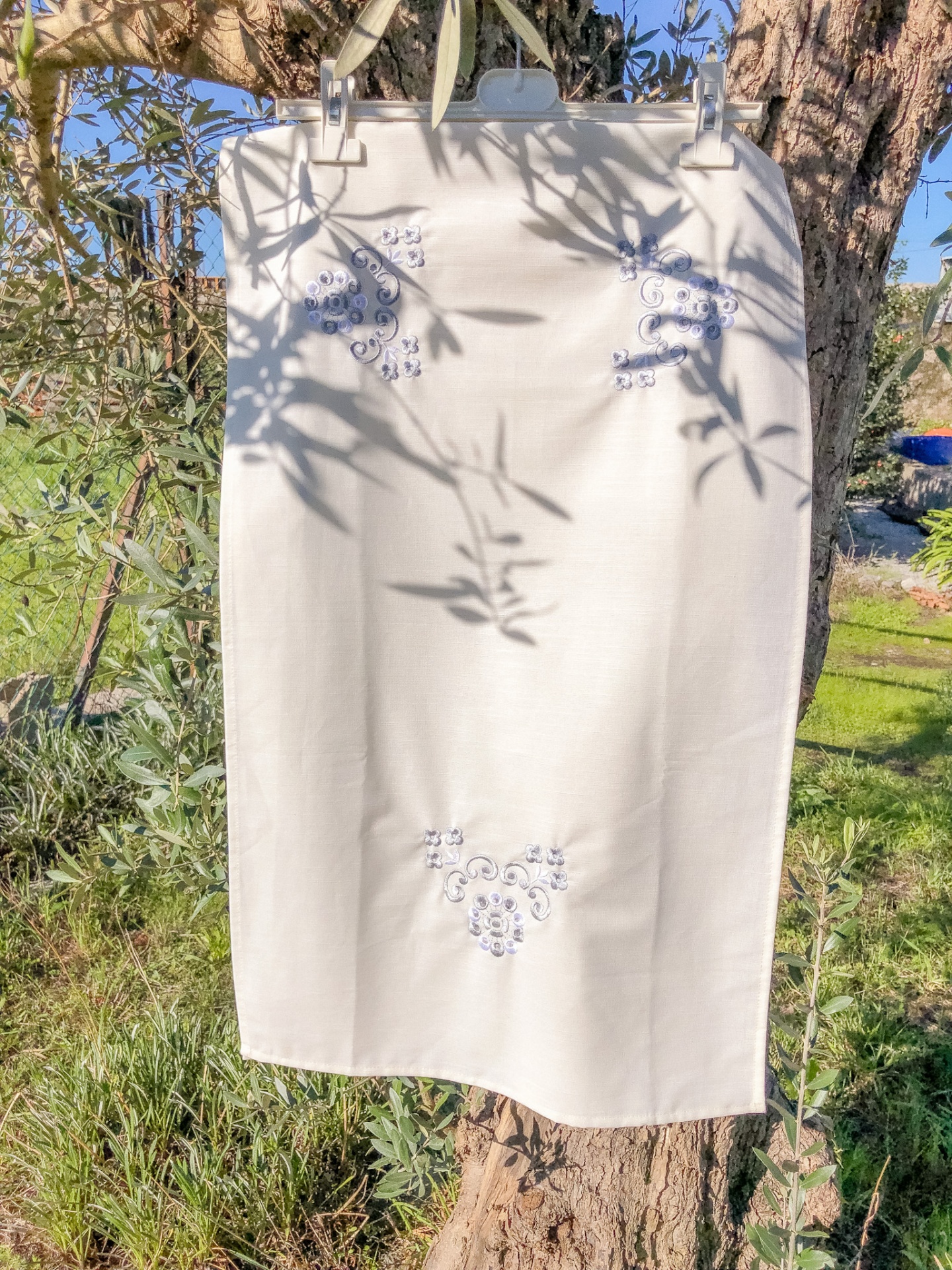 Saia branca bordada pendurada numa árvore ao ar livre