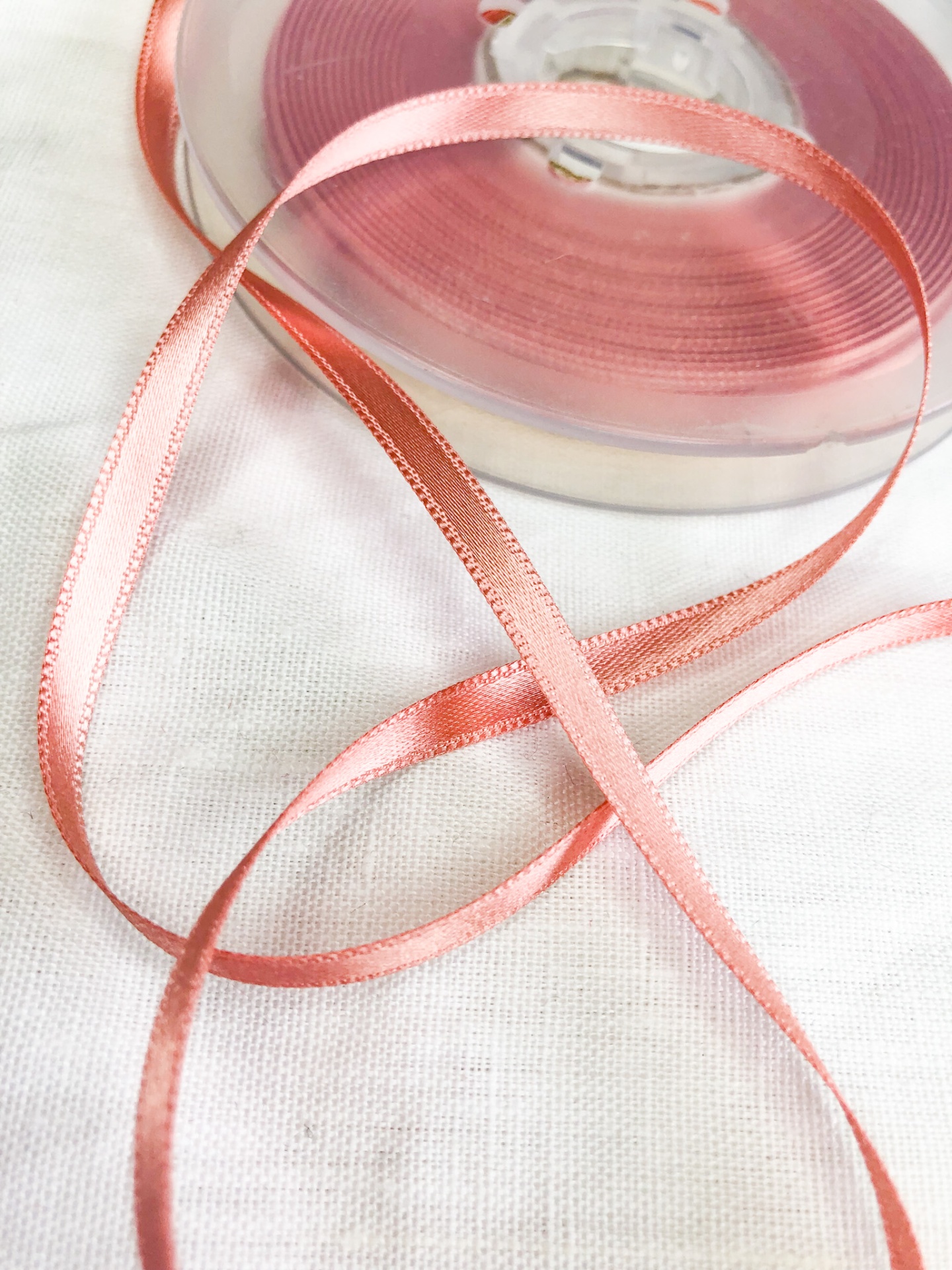 Fita de cetim cor salmon em bobina sobre tecido branco