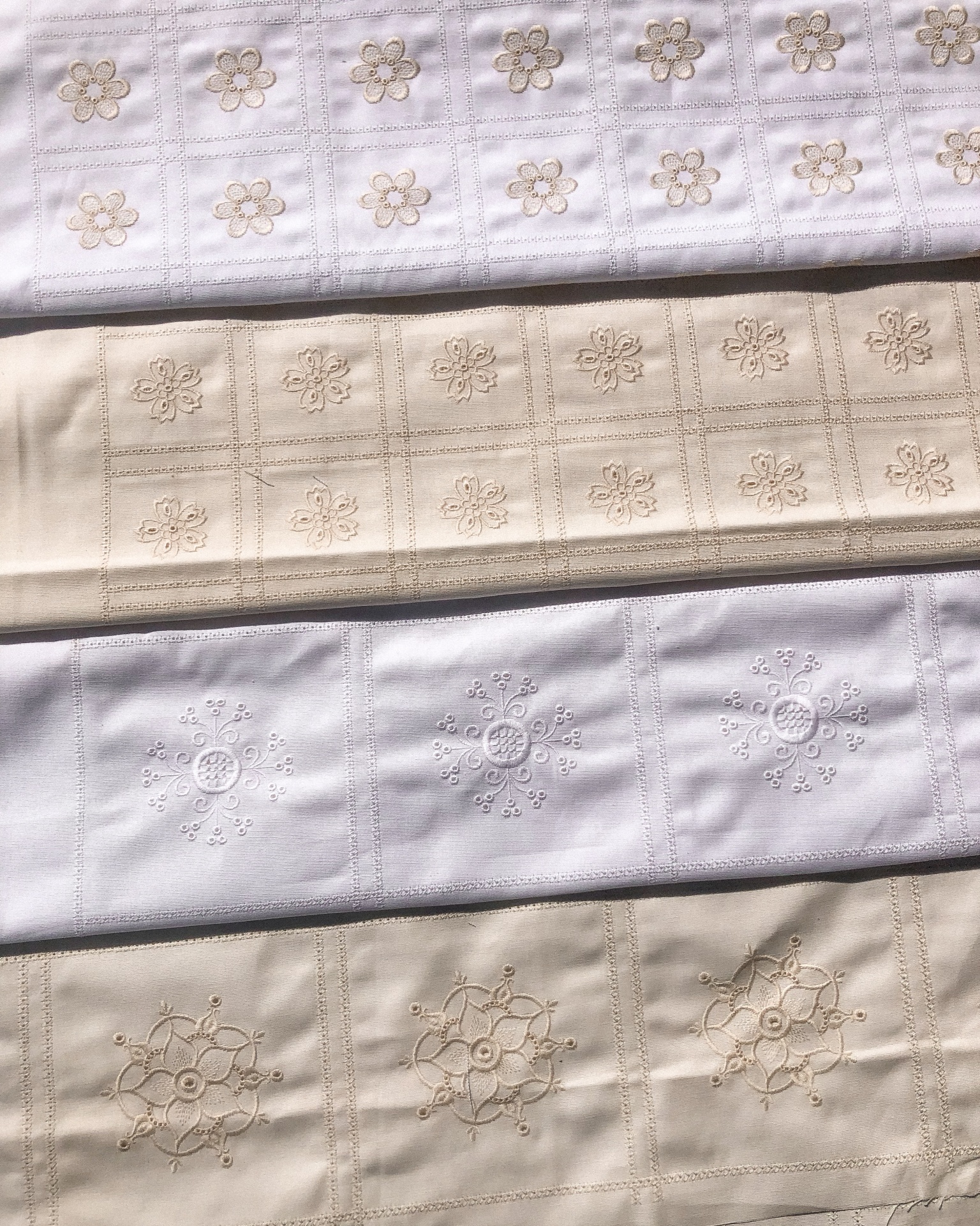 Tecidos bordados brancos e bege com padrões florais em quadrados