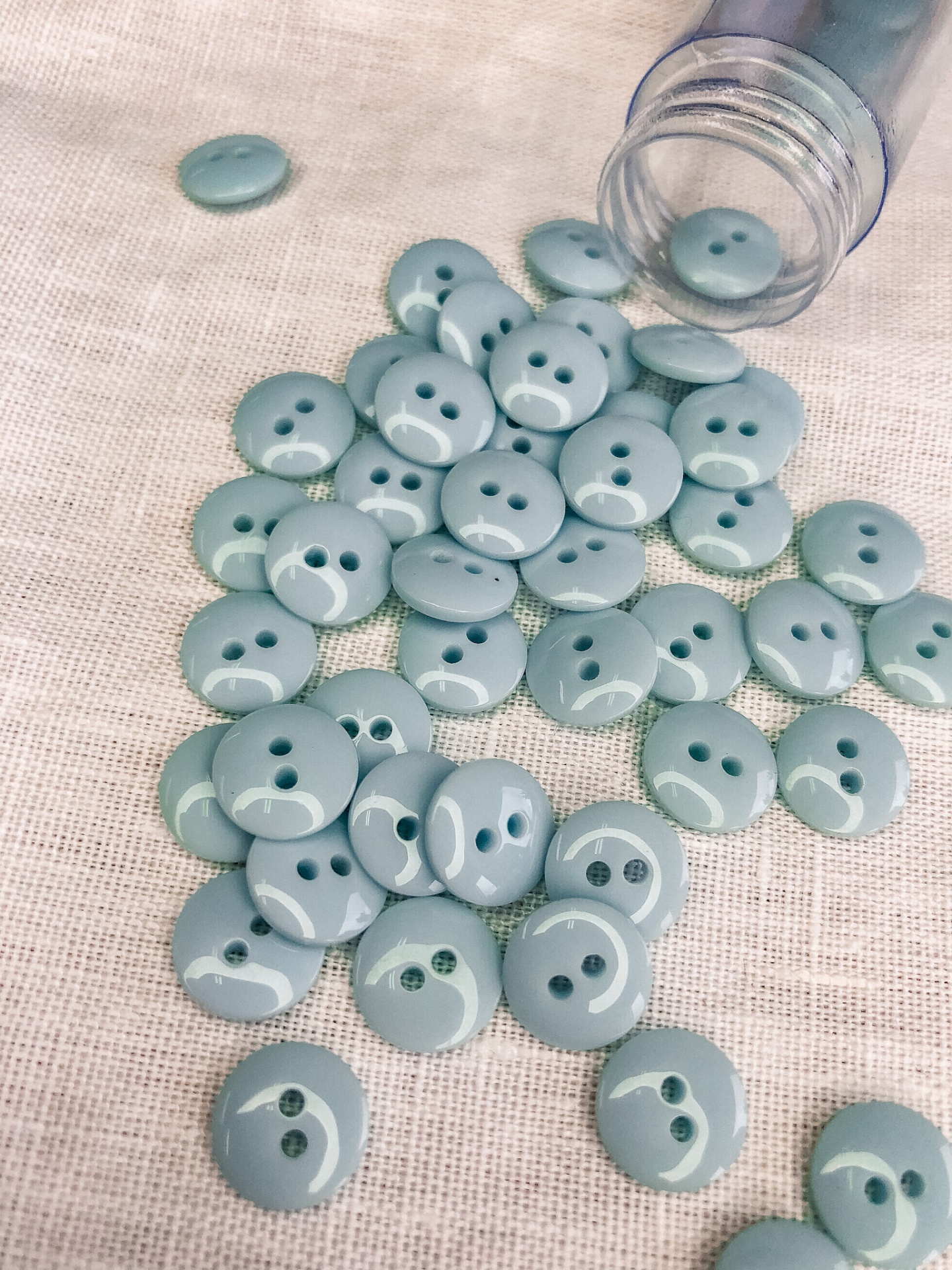 Botões redondos verdes em tecido bege ao lado de recipiente plástico.