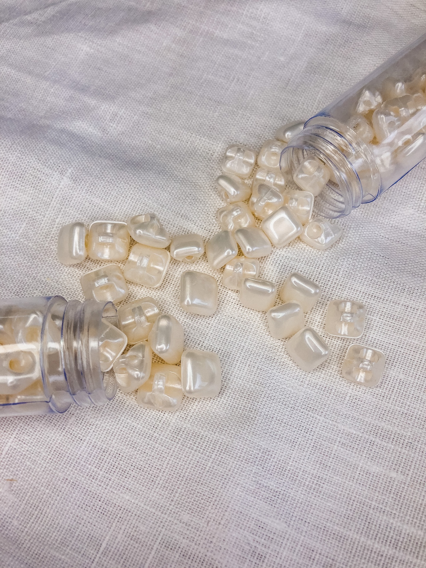 Contas de cor pérola espalhadas sobre tecido branco com duas embalagens plásticas abertas