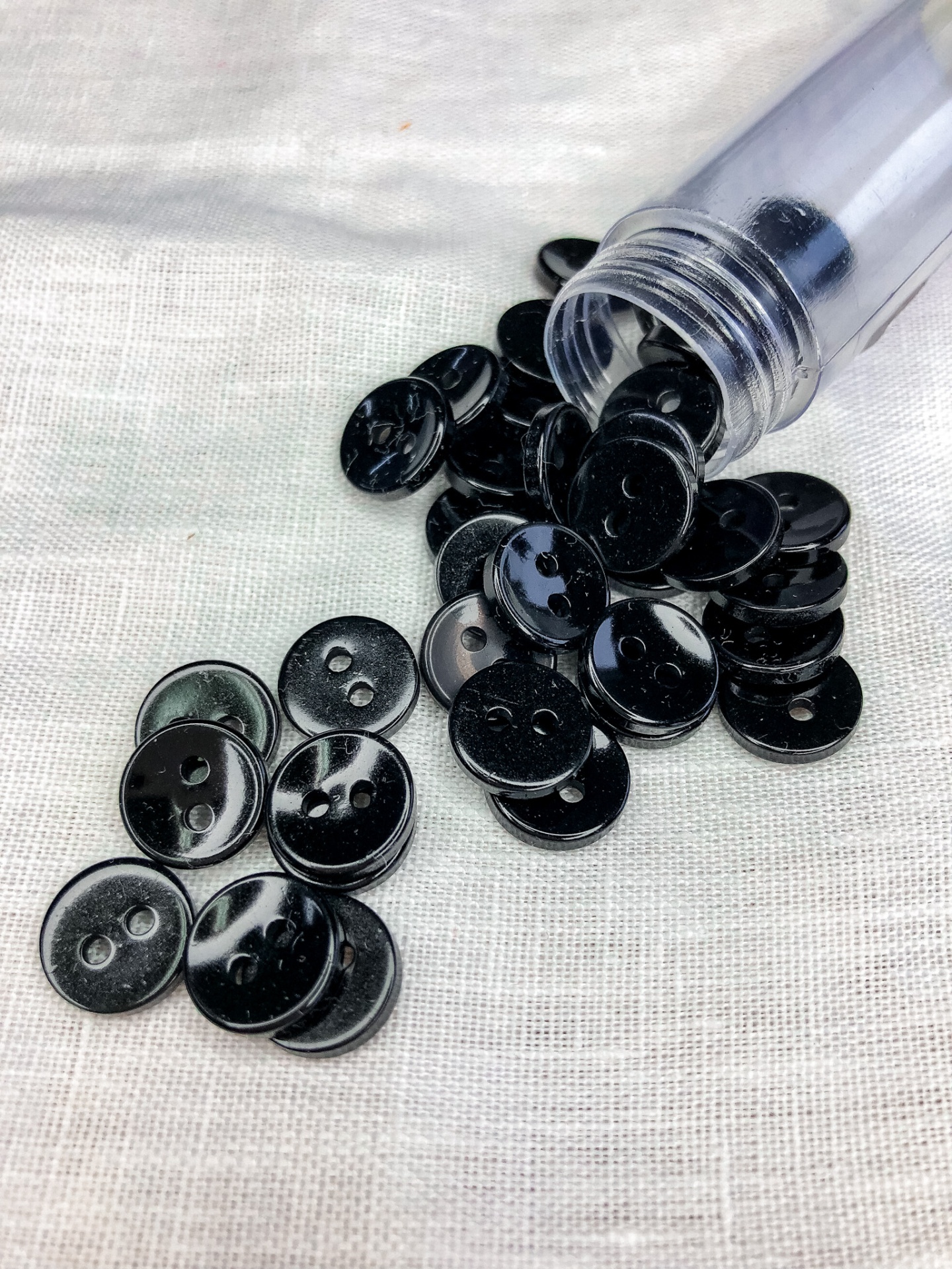 Botões pretos brilhantes com dois furos espalhados e frasco transparente inclinado