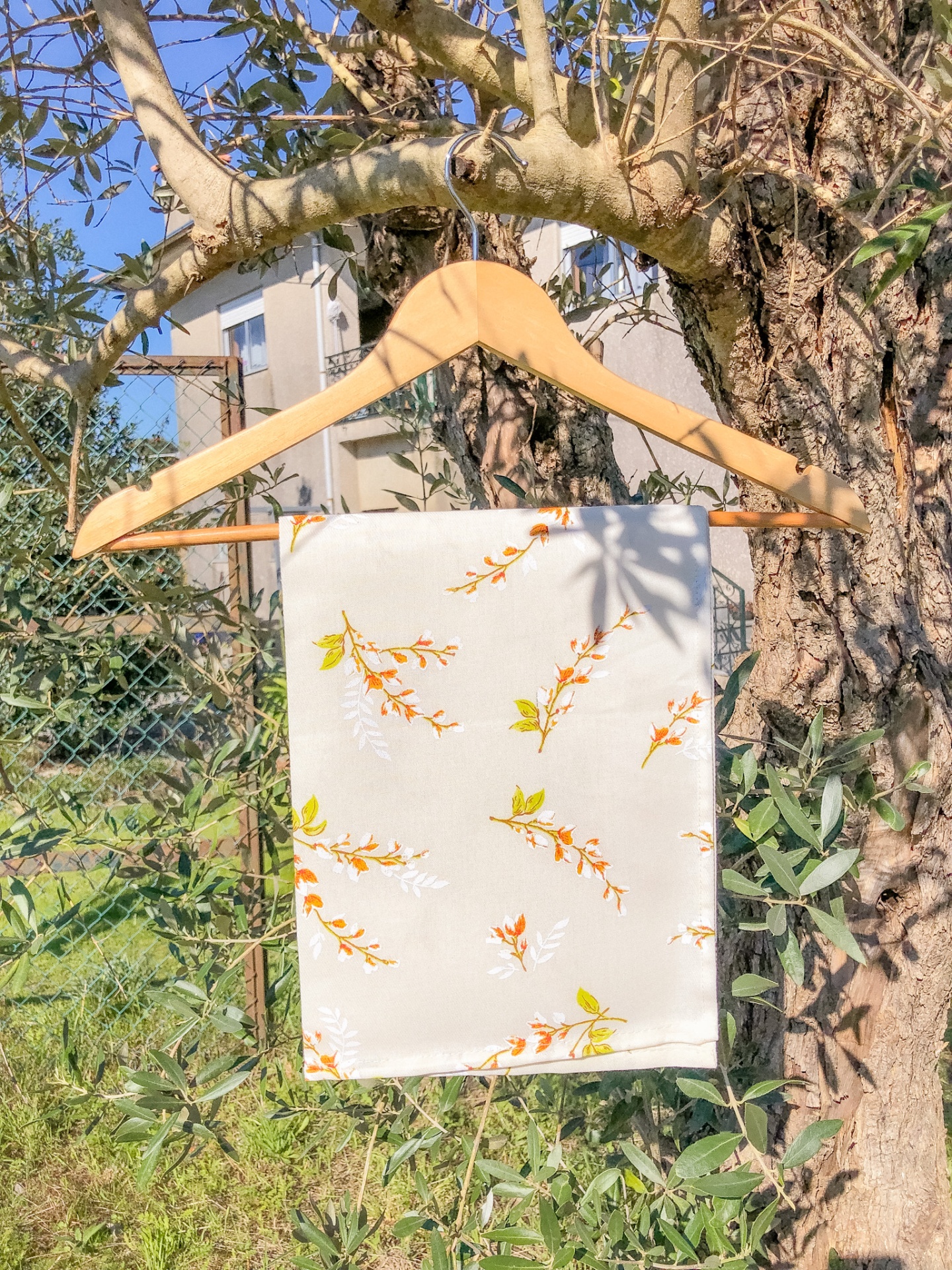 Toalha bege com padrão floral pendurada em cabide de madeira numa oliveira