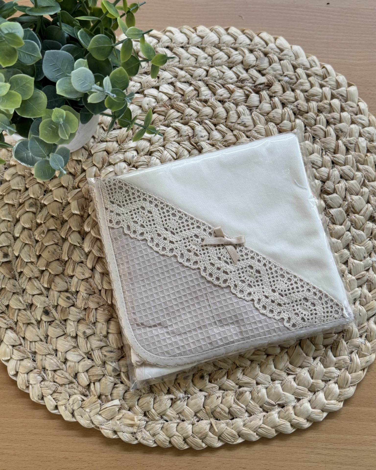 Toalha branca com renda e laço sobre base trançada com planta verde