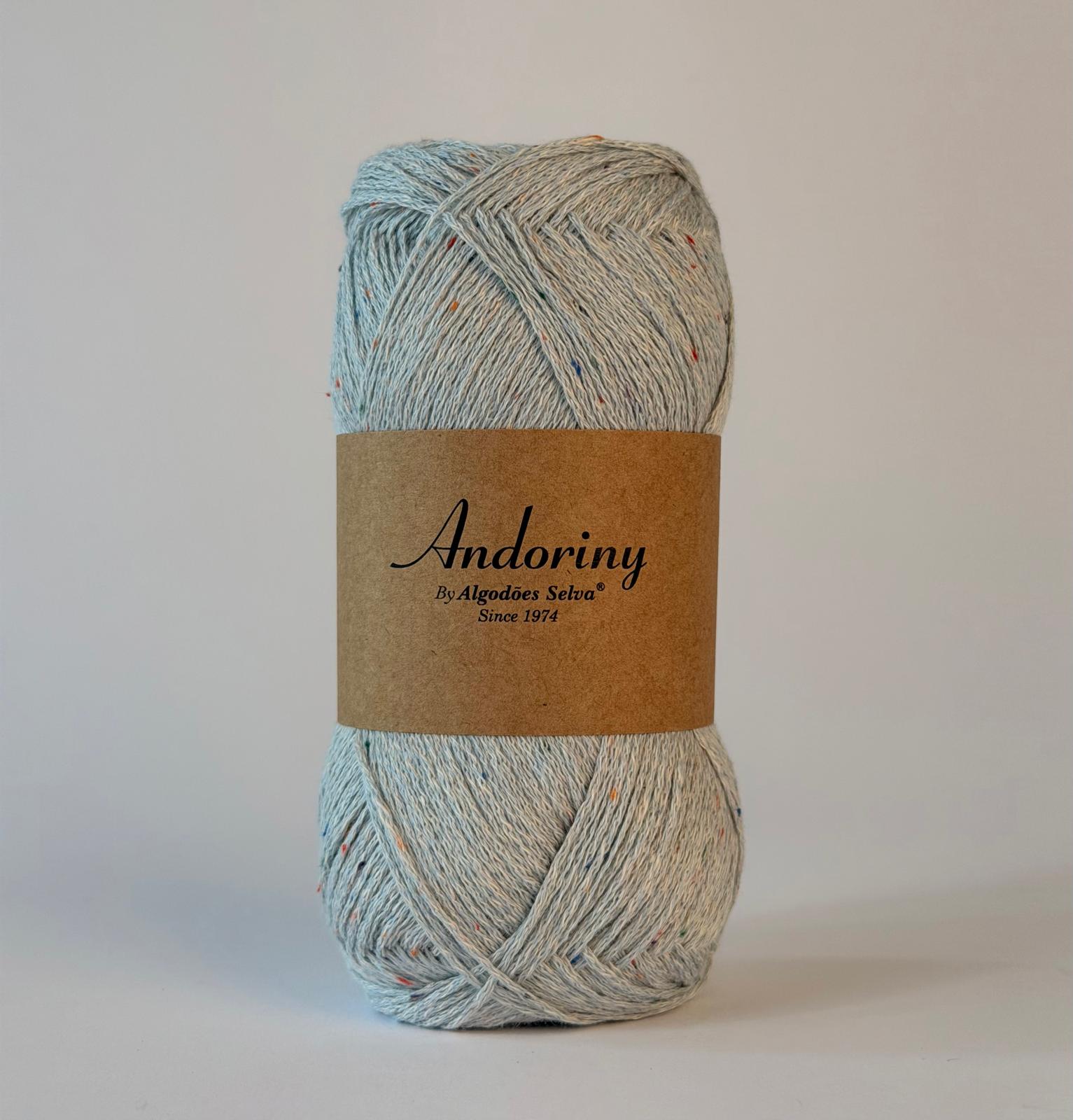 Novelo de fio azul claro com rótulo castanho e texto preto sobre fundo branco