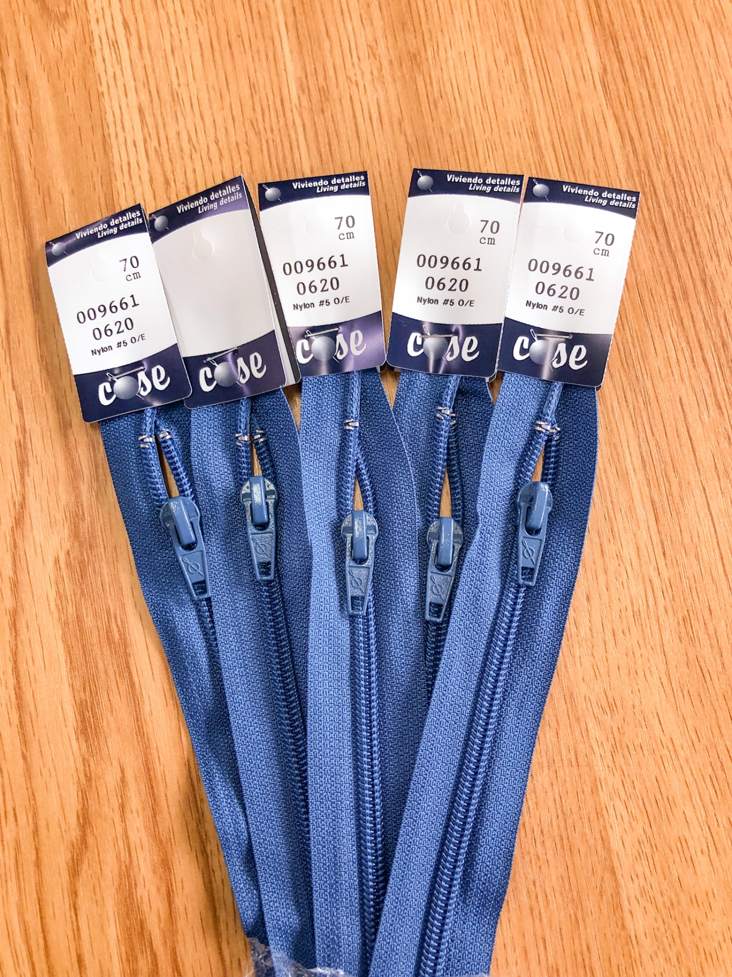 Cinco fechos éclair azuis com etiquetas sobre uma superfície de madeira clara