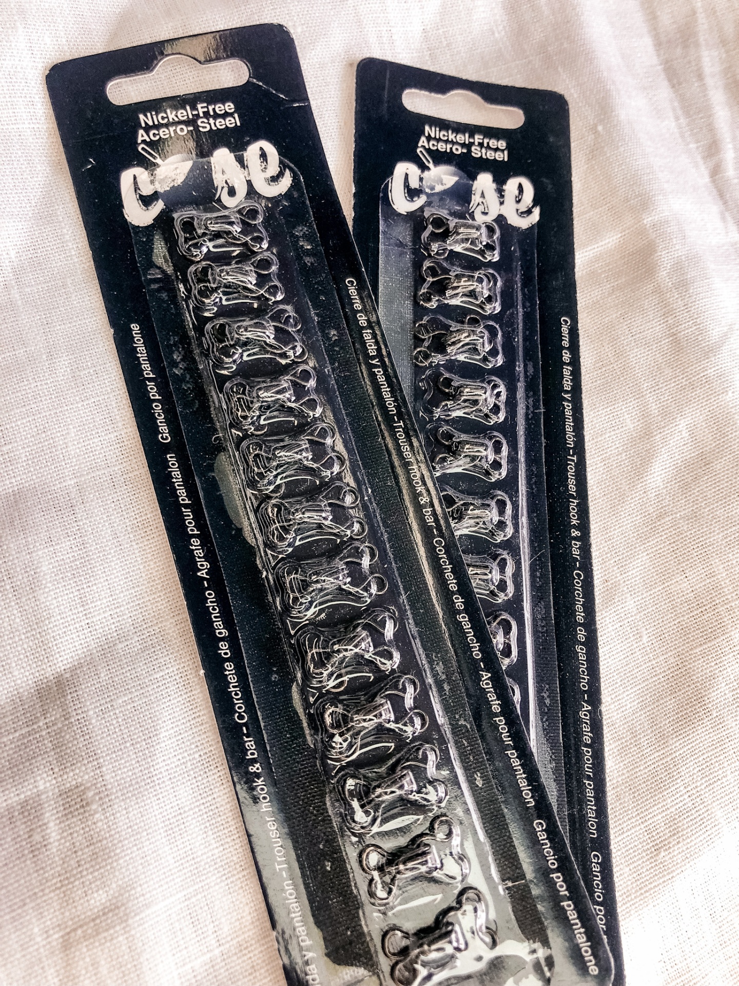 Dois conjuntos de ganchos de metal prateados em embalagem preta