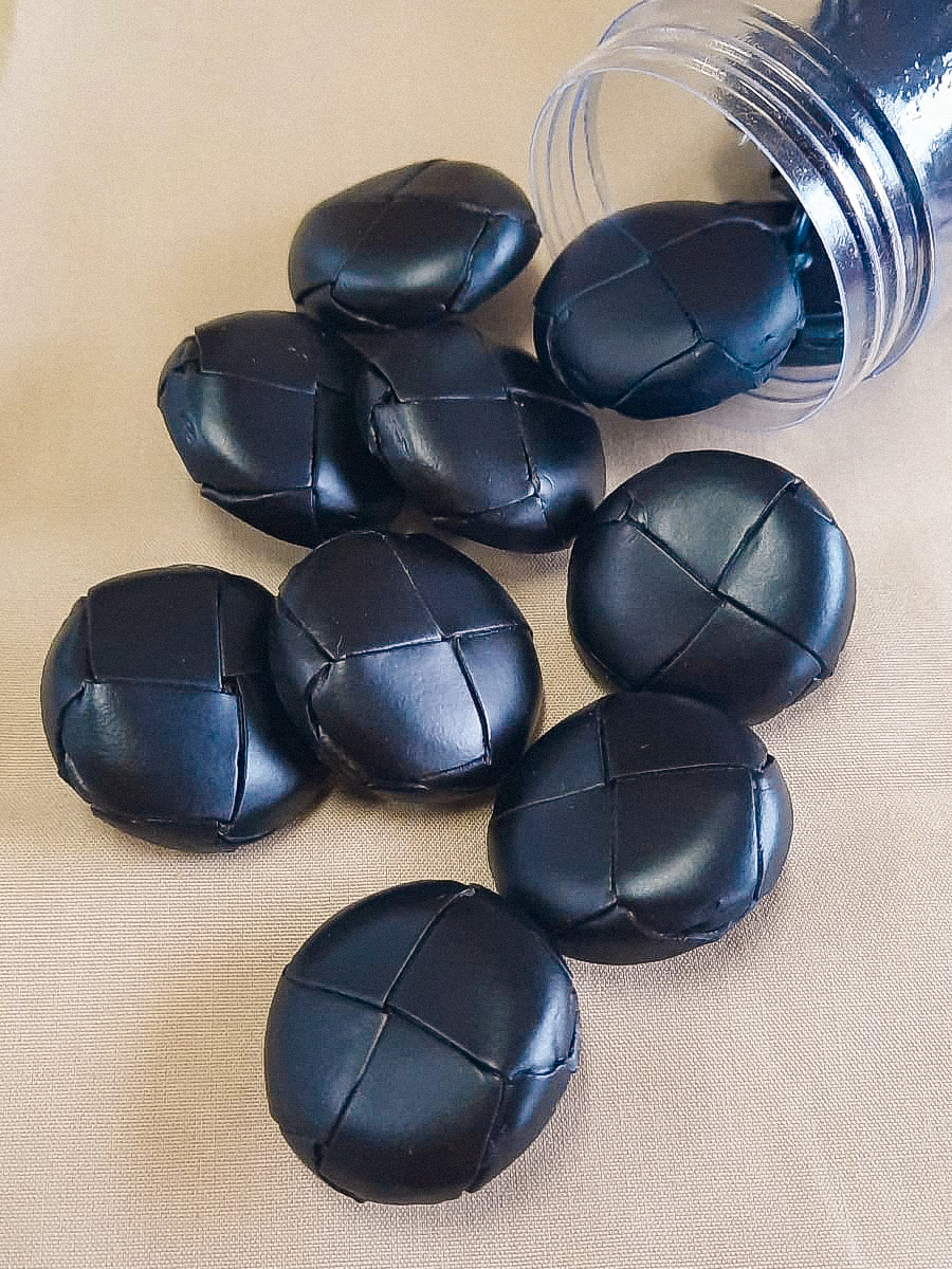 Botões redondos negros com relevo em cruz, sobre superfície bege e dentro de pote plástico