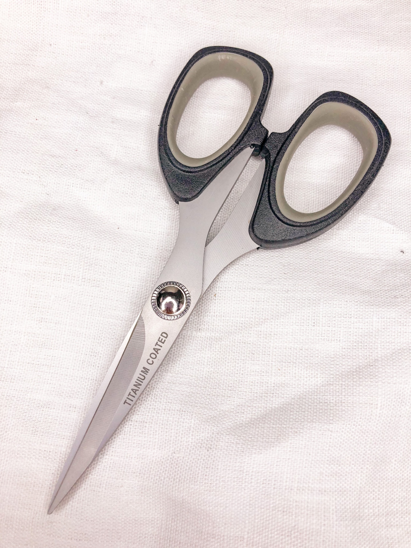 Tesoura com lâminas revestidas a titânio e cabos pretos e bege sobre tecido branco