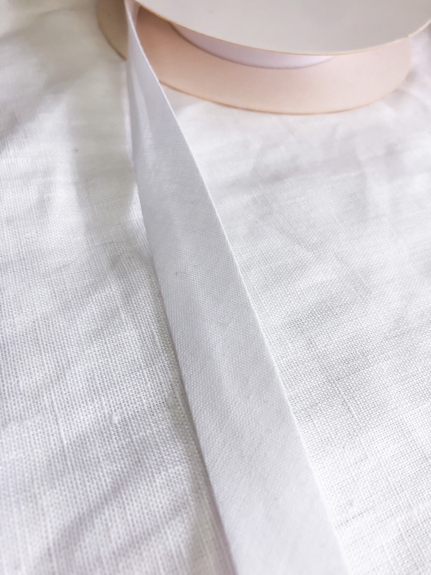 Rolo de fita de cetim cor bege claro sobre tecido branco