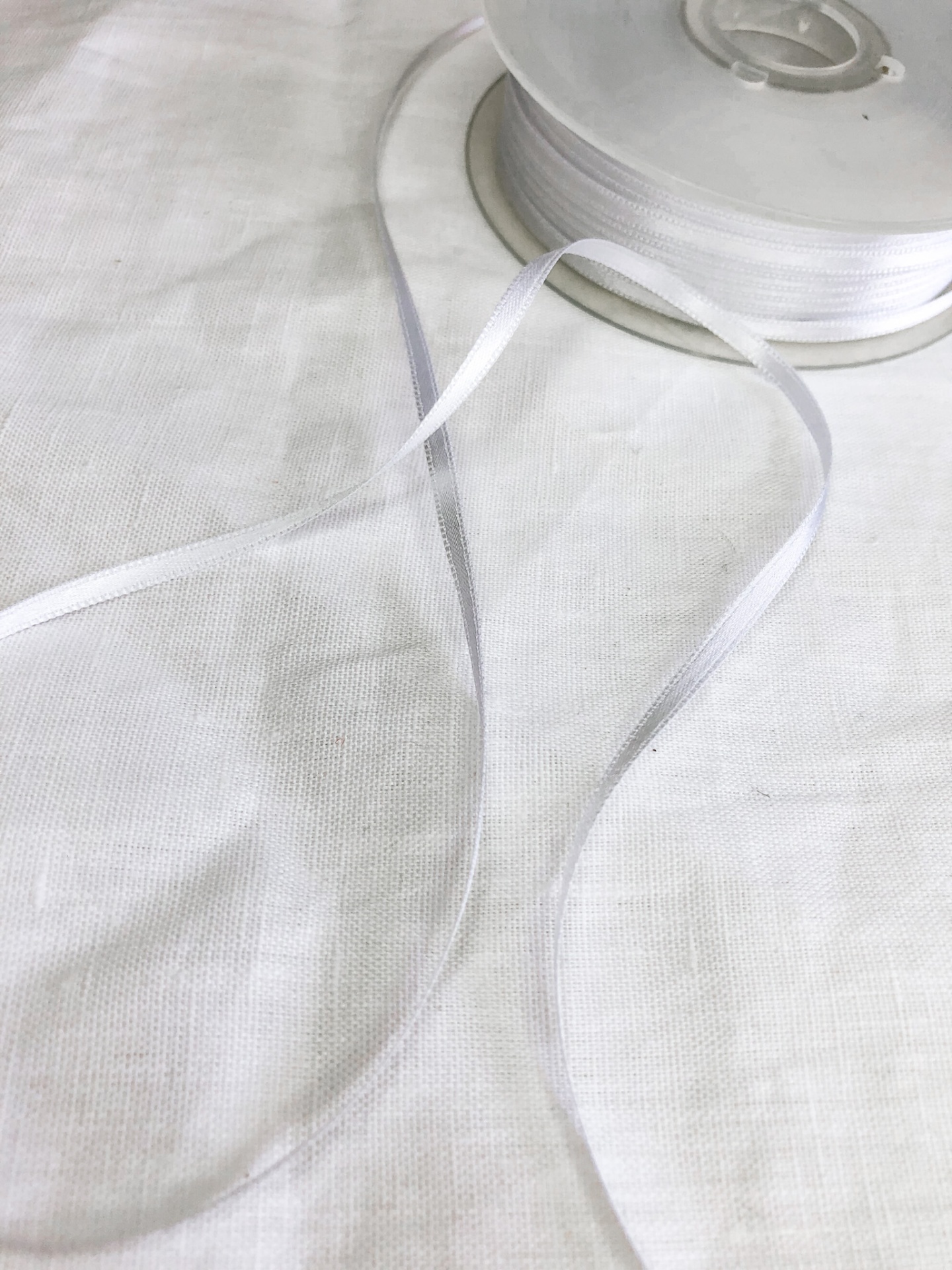 Rolo de fita branca fina em material sintético sobre tecido branco