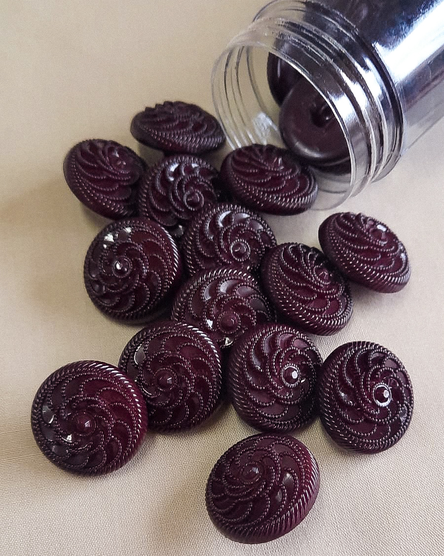 Botões bordô redondos com padrão espiral em relevo ao lado de recipiente transparente