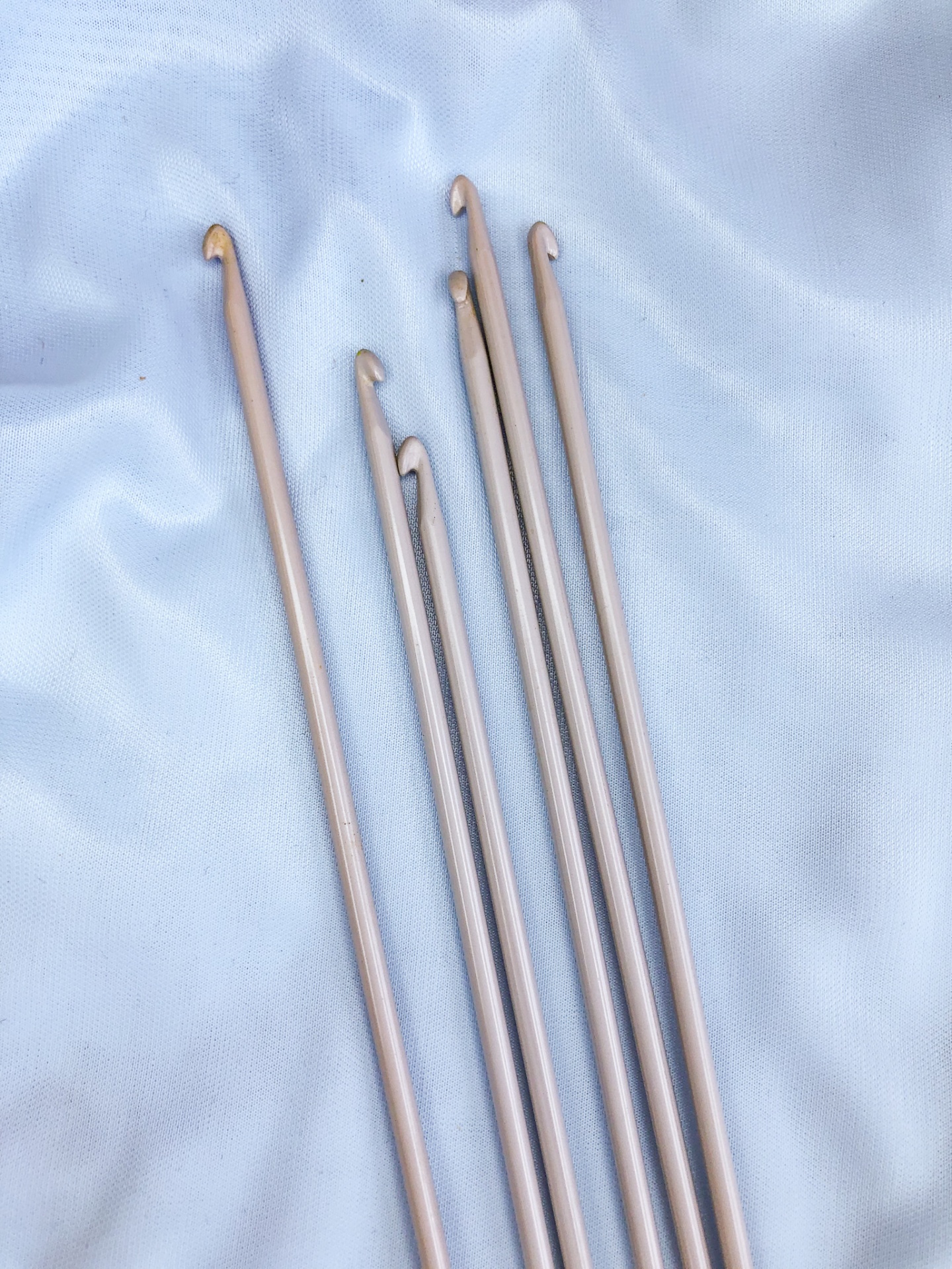 Seis agulhas de crochet metálicas prateadas sobre tecido branco