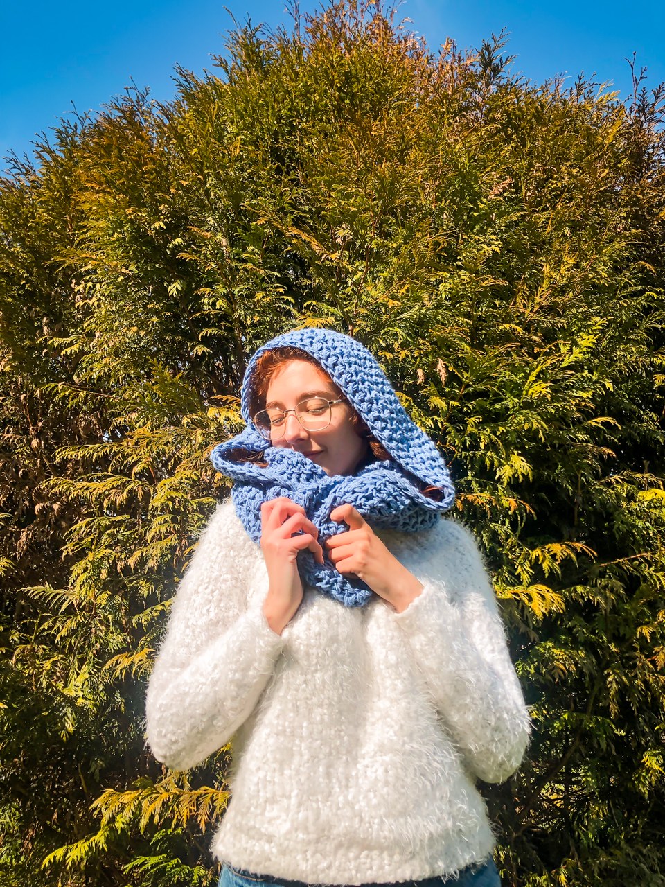 Mulher com suéter branco felpudo e cachecol de malha azul claro ao ar livre em dia de sol