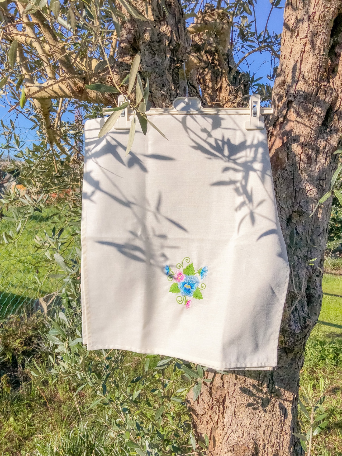 pano de cozinha branco com bordado de flores coloridas pendurado numa árvore