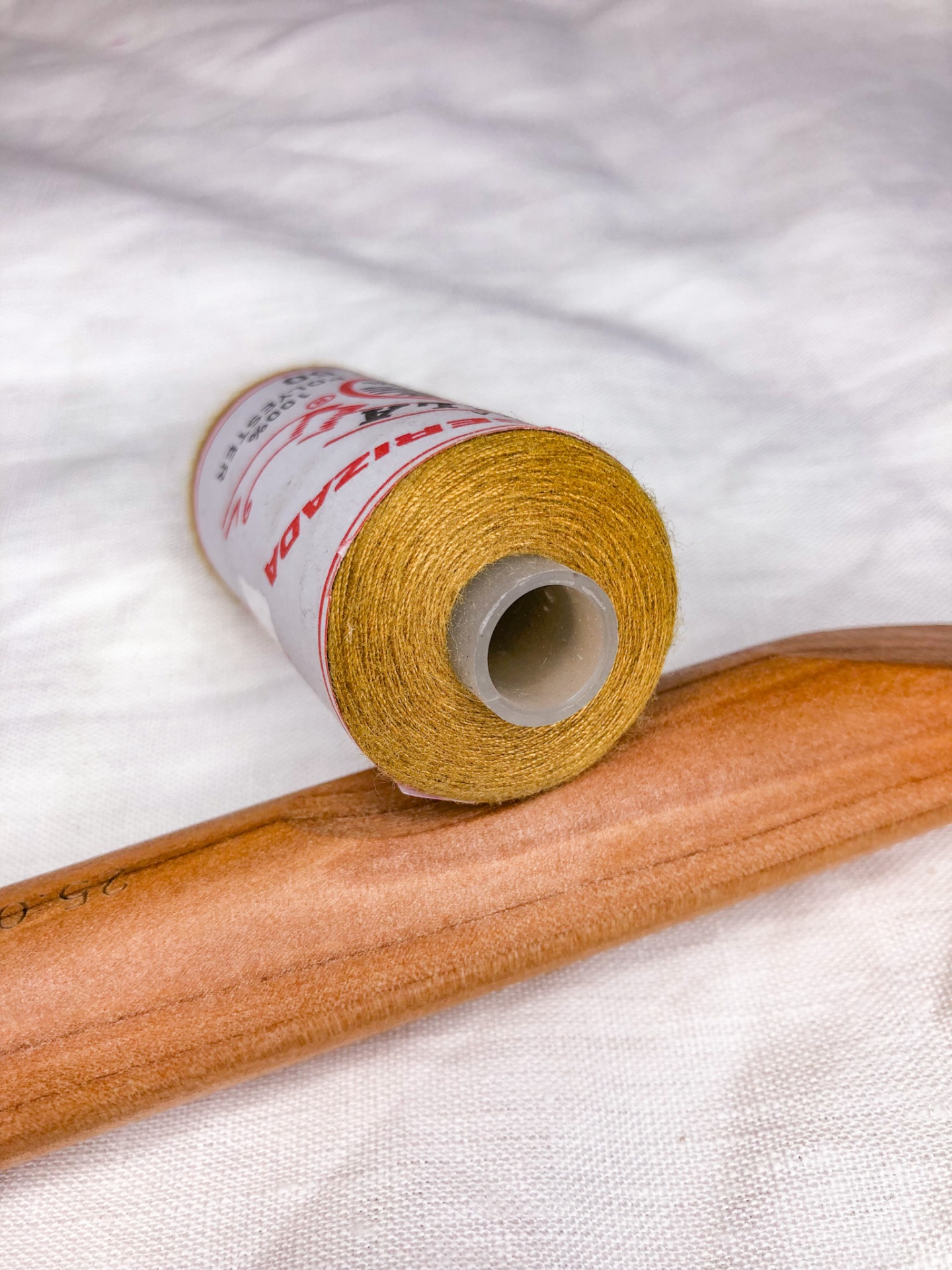 Rolo de linha dourada e cabide de madeira sobre tecido branco