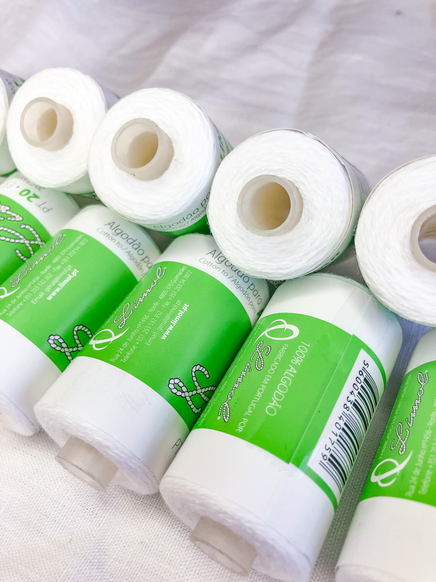 Carretéis de linha branca com rótulos verdes 'Algodão Puro' e código de barras.