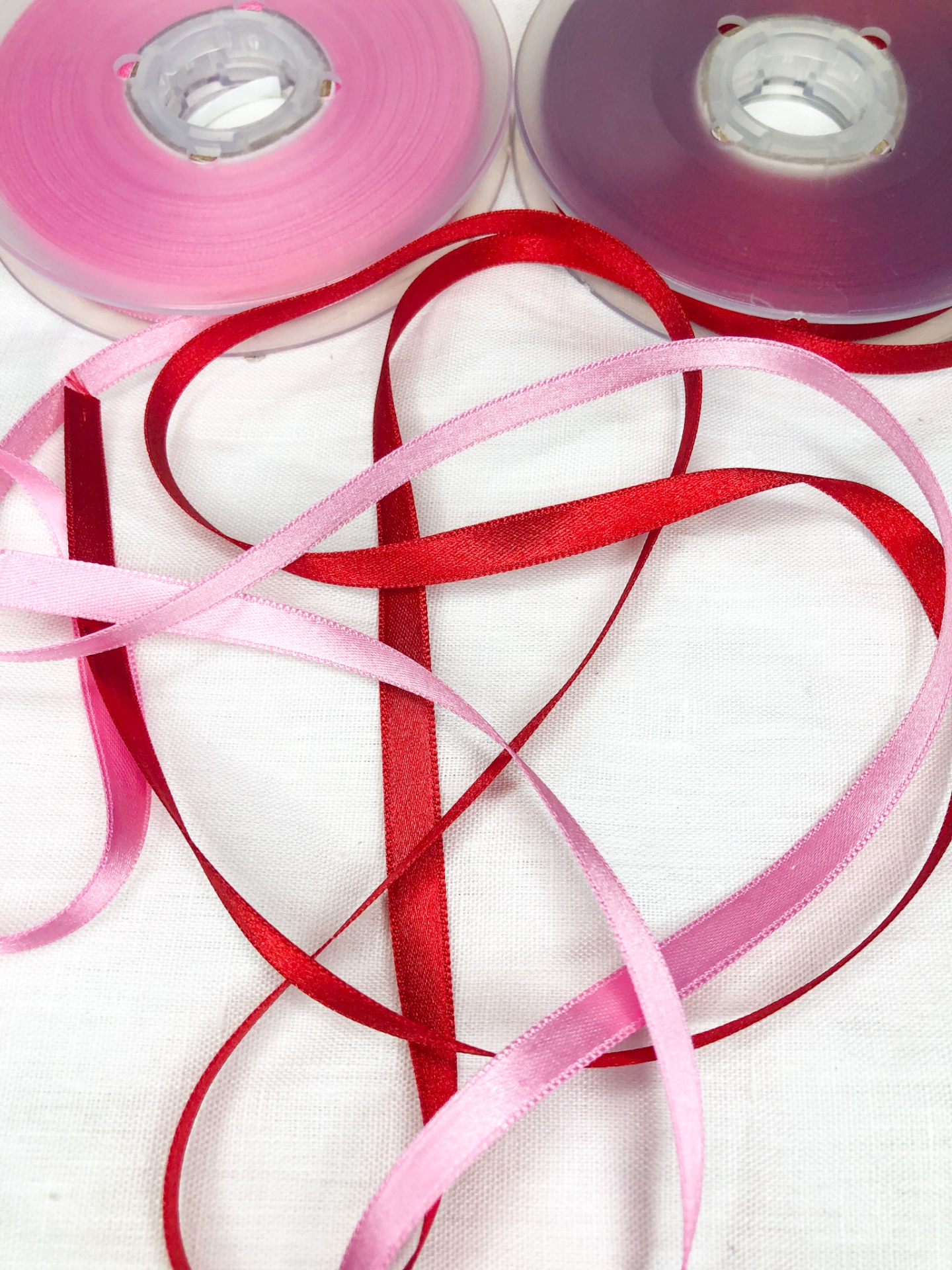 Rolos de fita de cetim rosa e roxo com fitas rosa e vermelha desenroladas sobre fundo branco