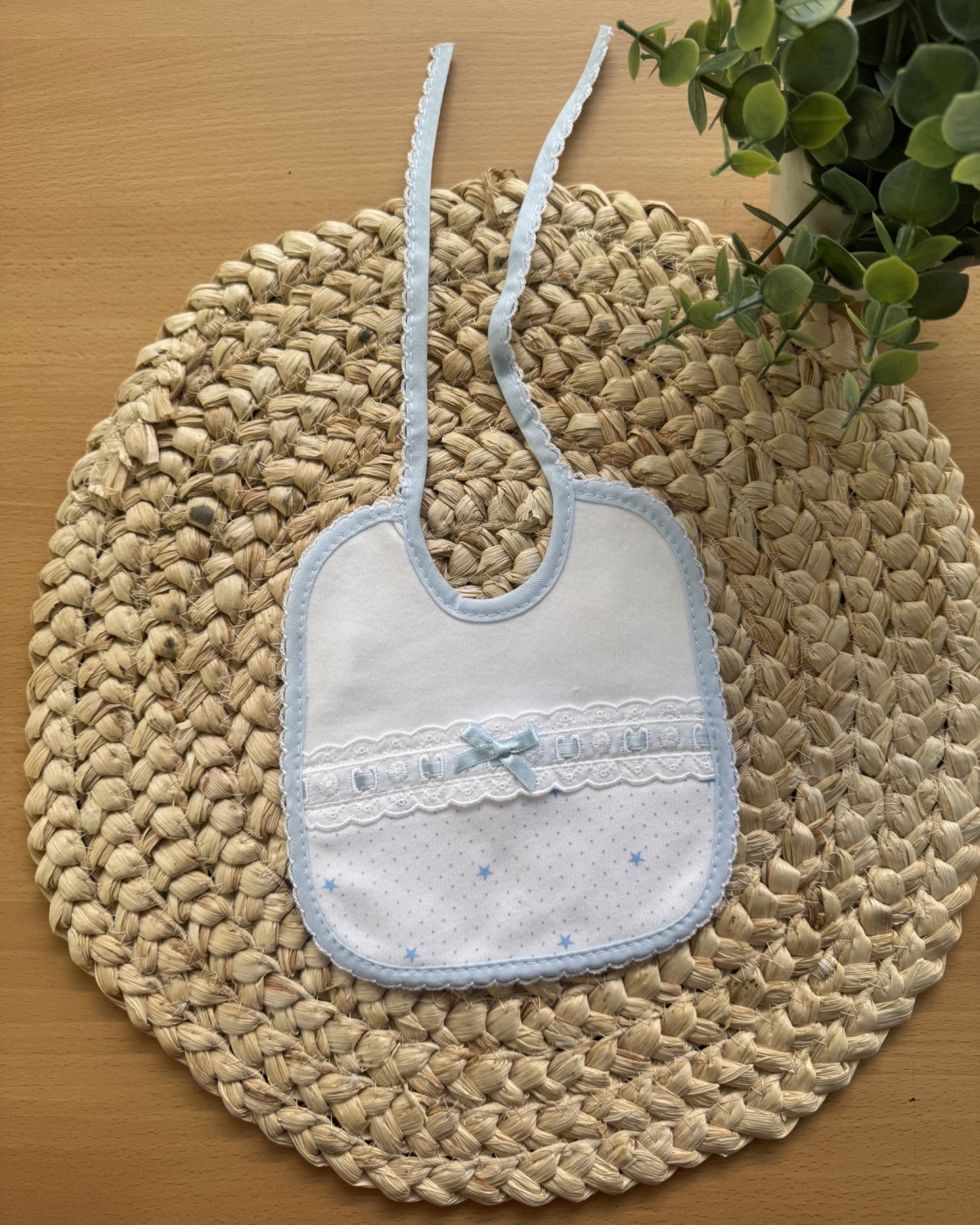 Babete branco e azul claro com padrão de estrelas e laço em tecido sobre base trançada