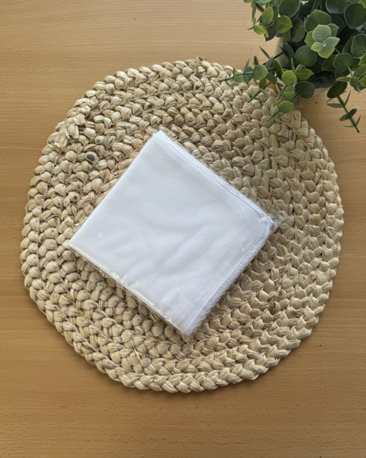 Guardanapo branco sobre toalha trançada redonda em mesa de madeira com planta verde
