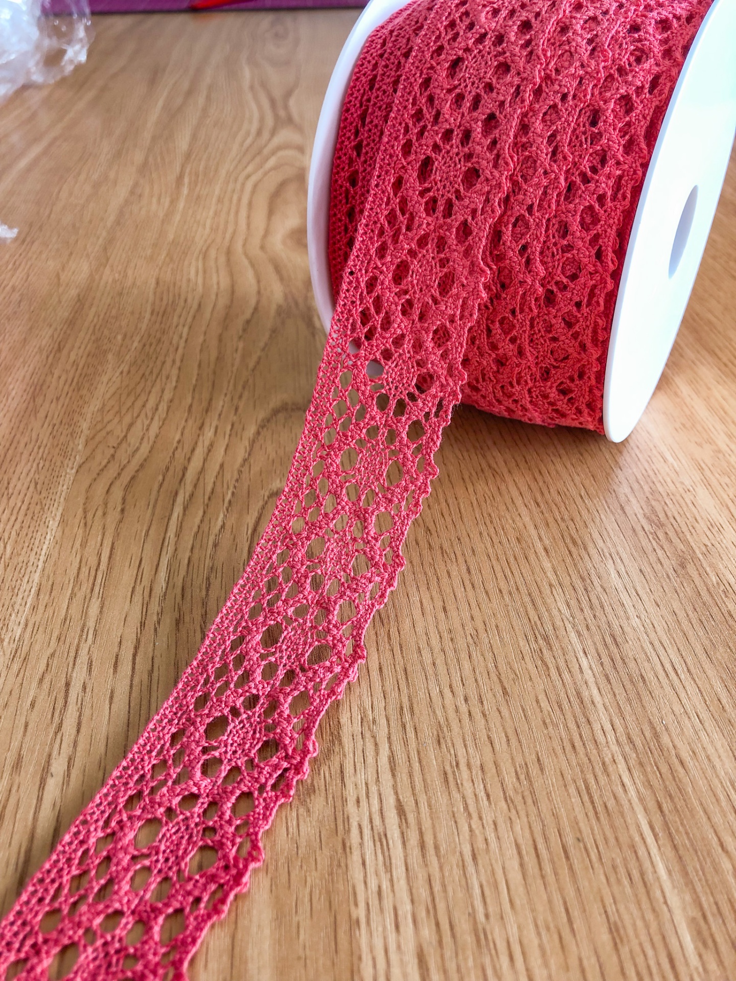 Rolo de renda vermelha com padrão floral em mesa de madeira clara