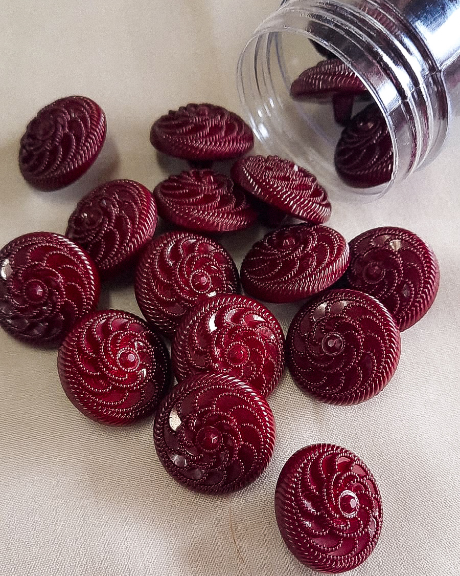 Botões bordô redondos com padrão espiral, frasco plástico e tecido claro