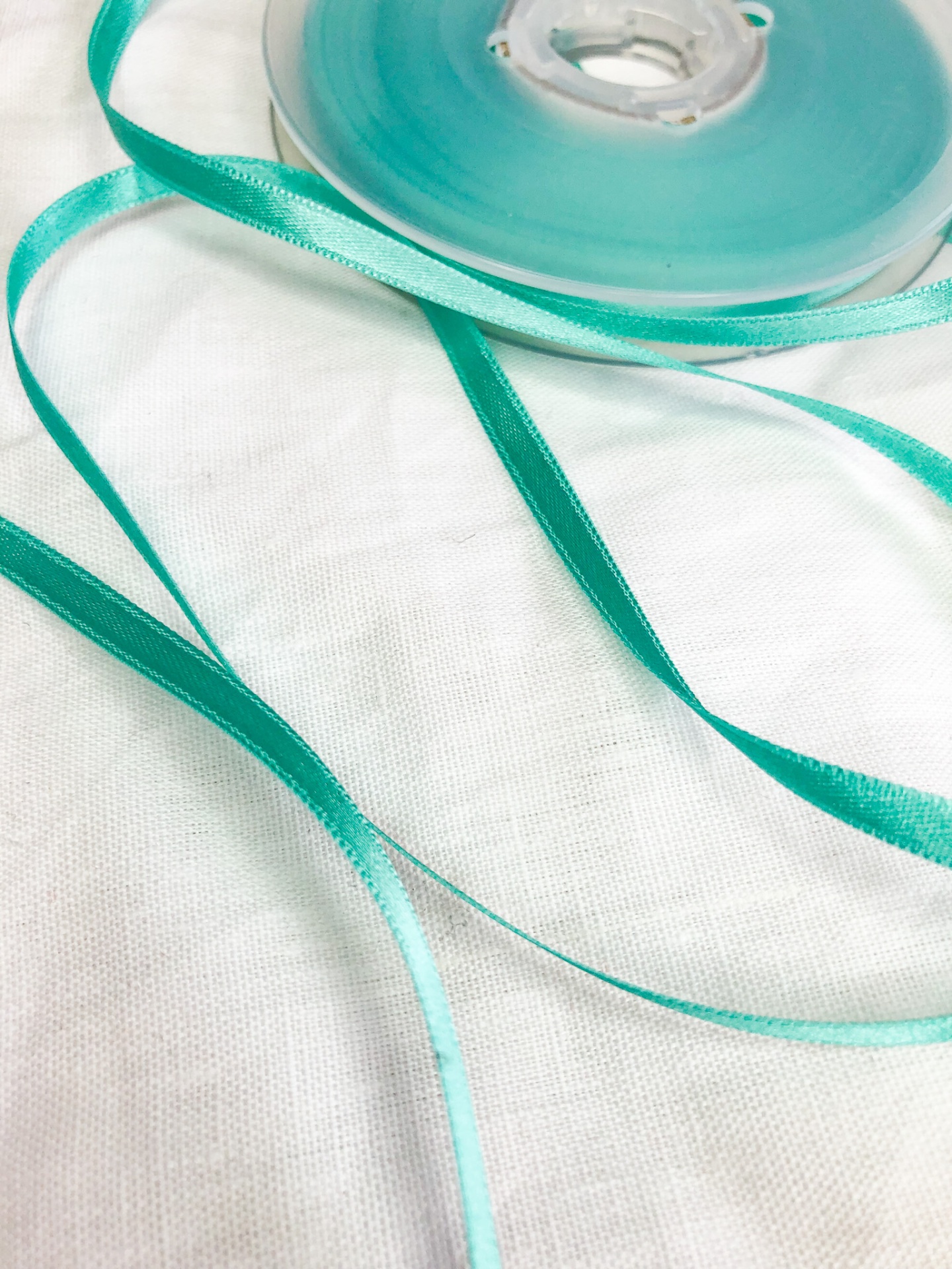 Fita de cetim azul-turquesa em rolo sobre tecido branco