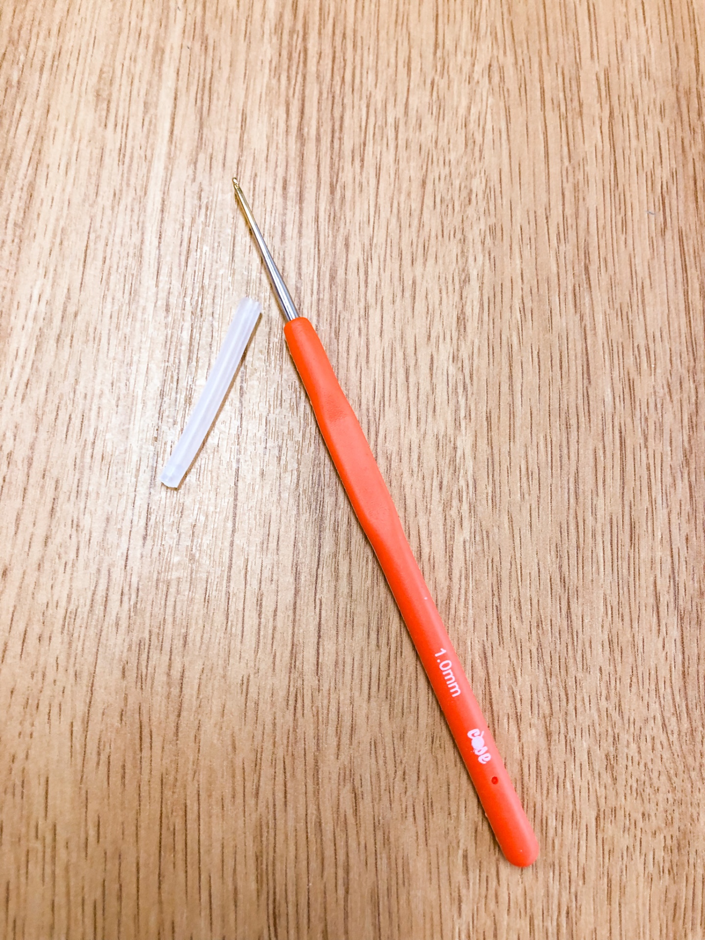 Agulha de crochet laranja com ponta metálica dourada e protetor branco sobre madeira
