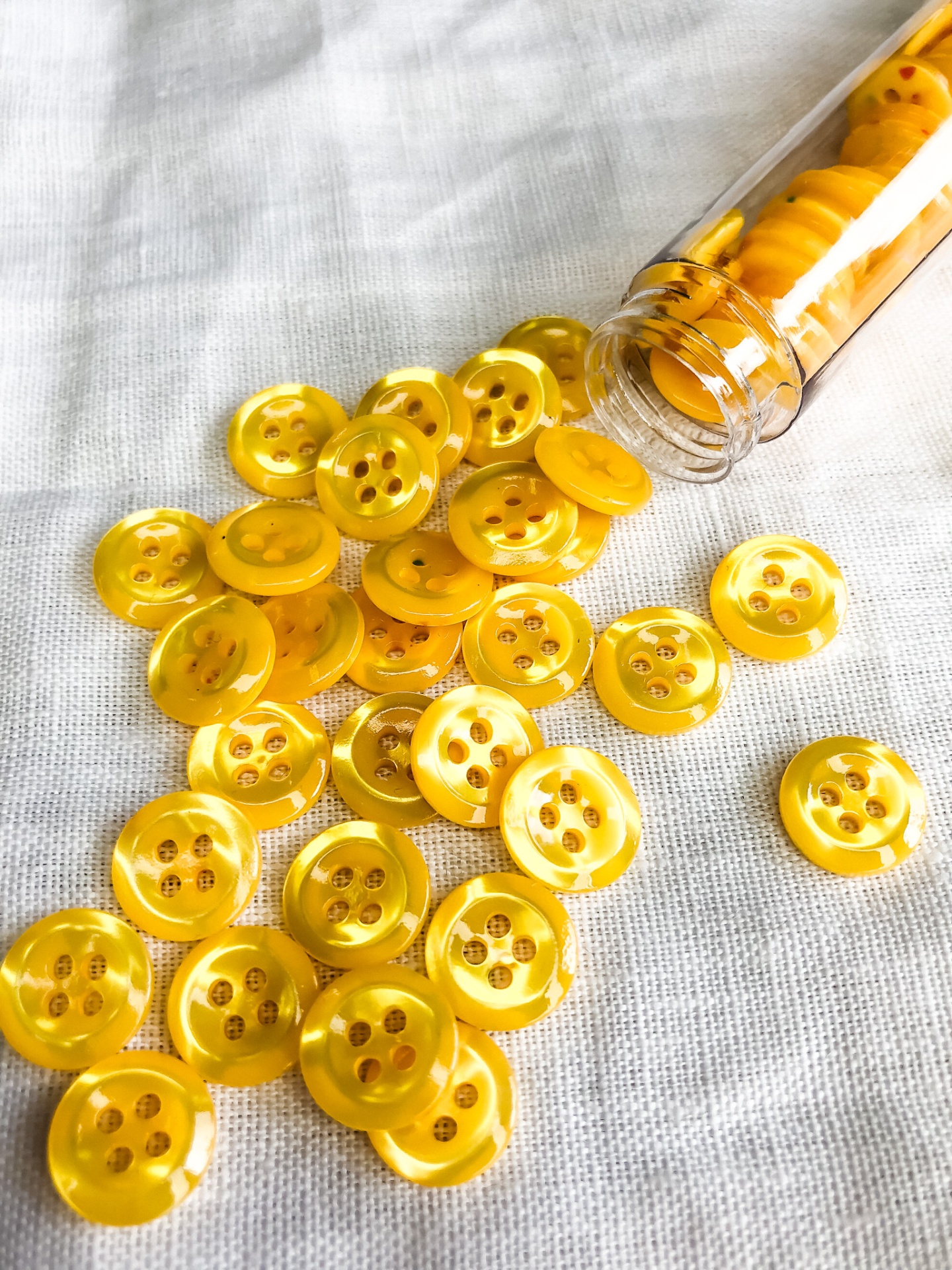 Botões amarelos de plástico com quatro furos em tecido branco e dentro de tubo de vidro
