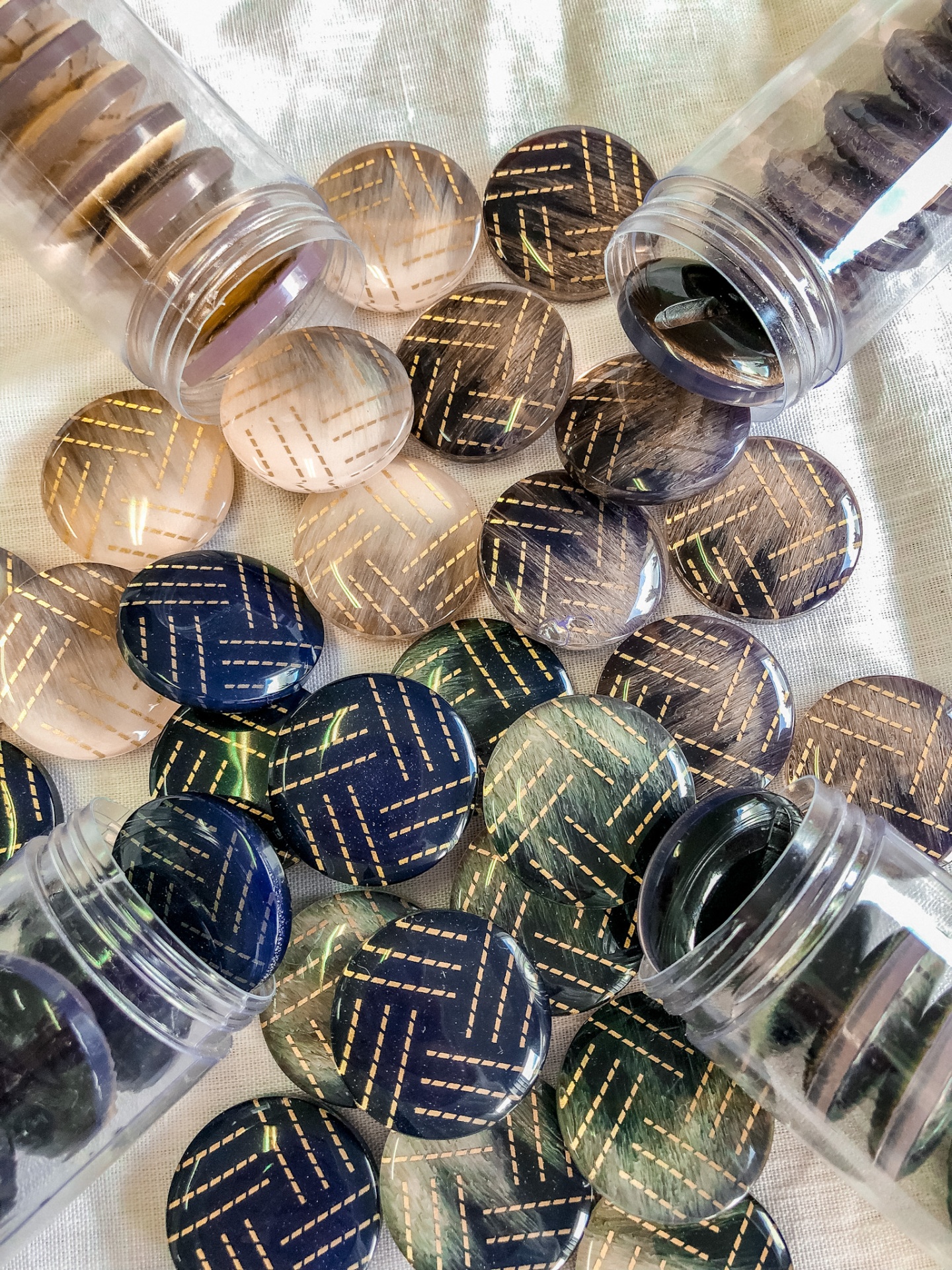 Botões redondos transparentes com padrão listrado dourado em cores variadas em frascos e sobre tecido branco