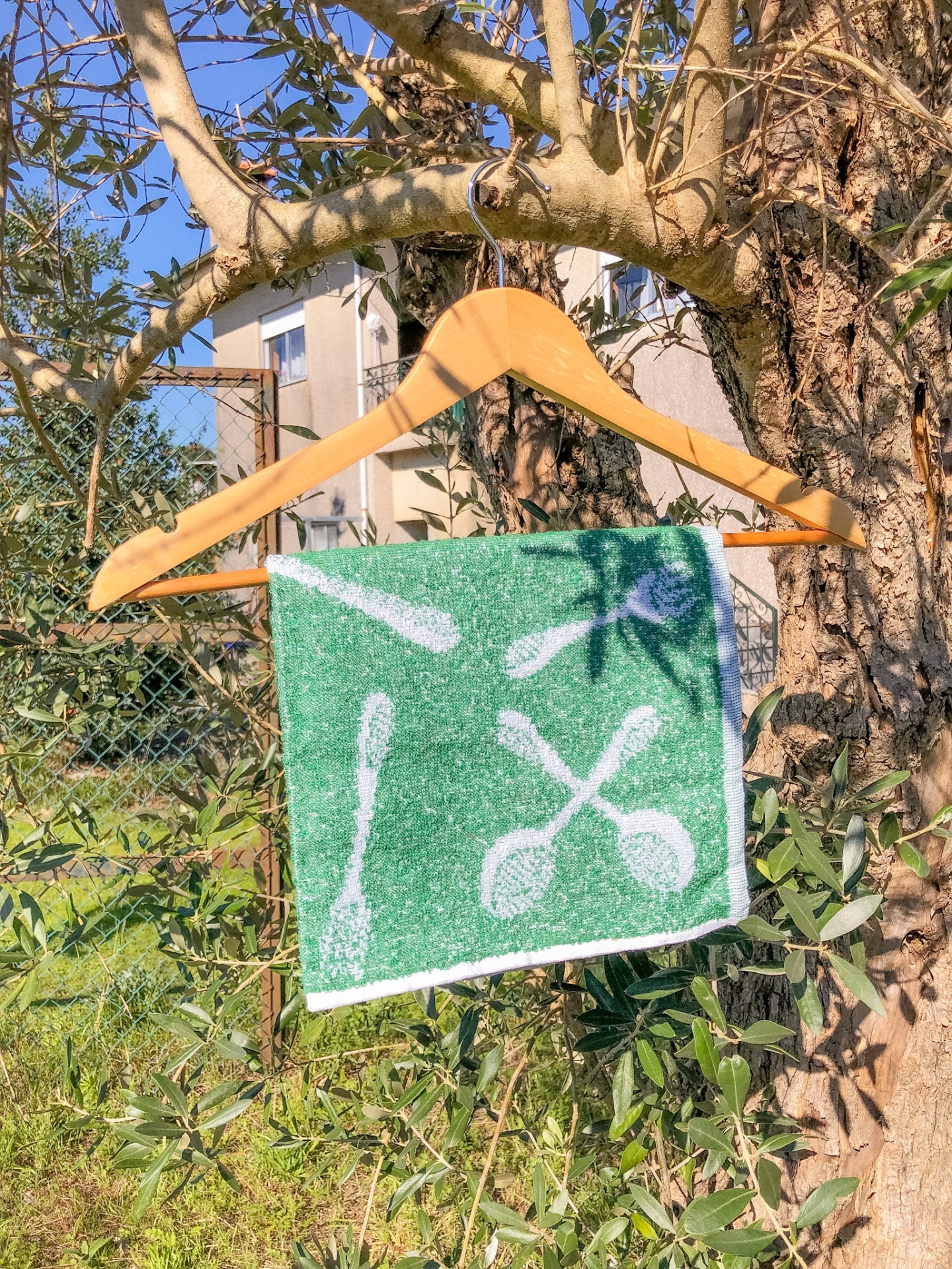 Toalha verde com desenhos brancos de utensílios de cozinha pendurada num cabide de madeira ao ar livre