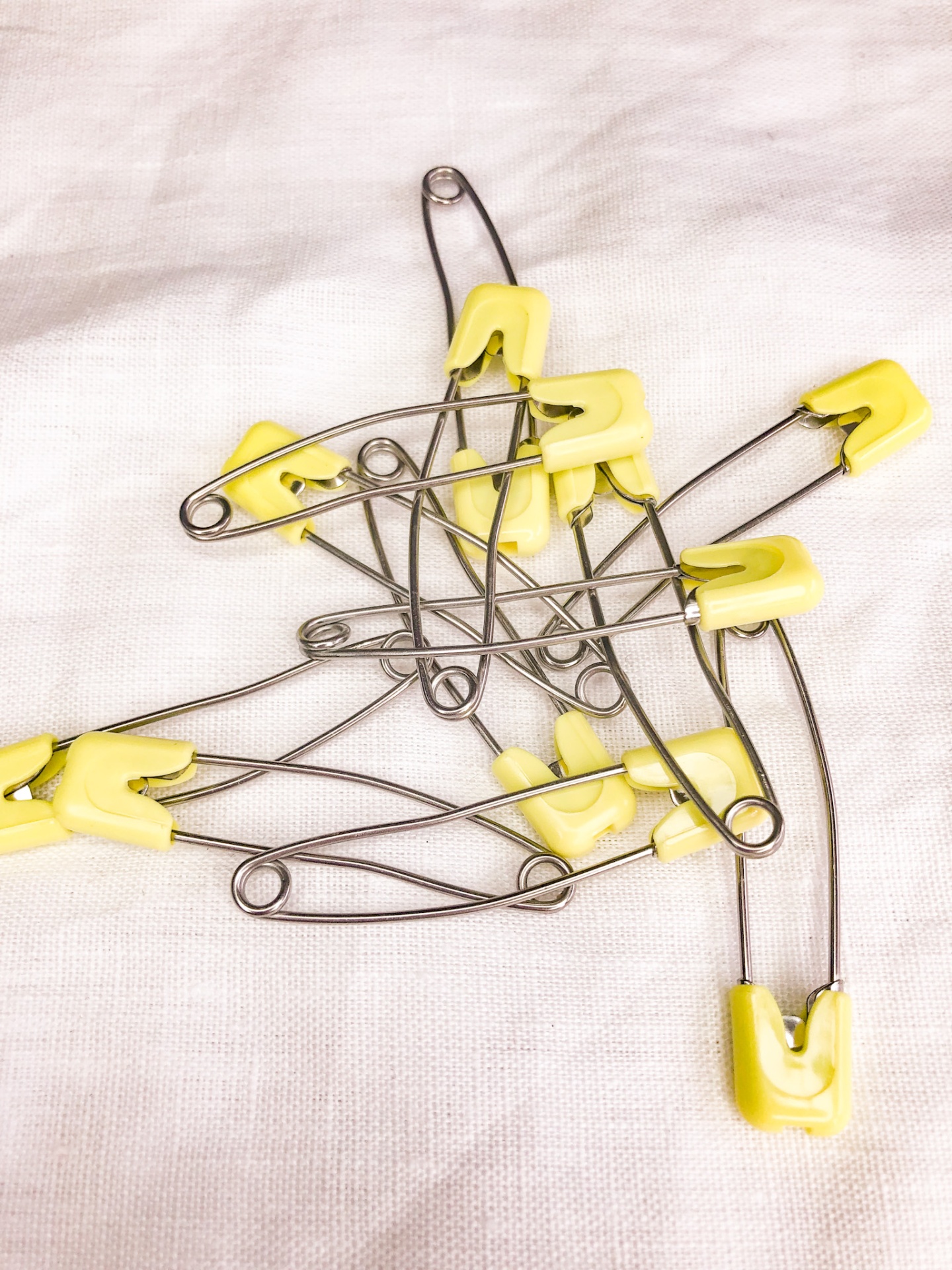 Vários alfinetes de segurança metálicos com ponta amarela sobre pano branco.