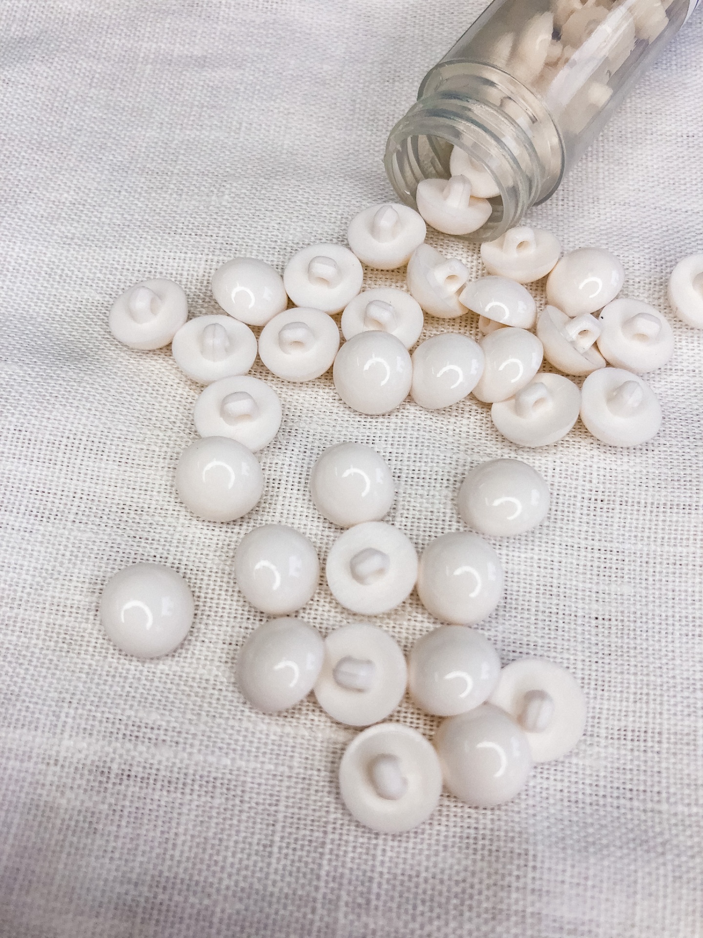 Miçangas brancas redondas em tecido branco próximo a frasco de vidro aberto