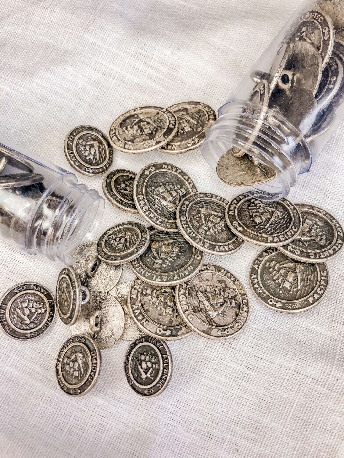 Moedas metálicas prateadas com inscrições U.S. NAVY PACIFIC espalhadas sobre tecido branco