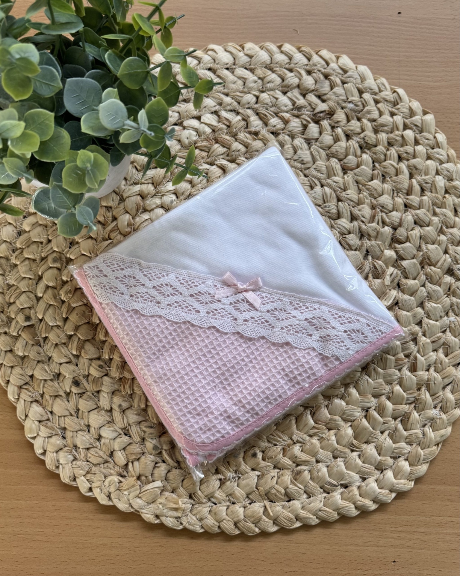 toalha branca com borda rosa e renda sobre base de corda trançada com planta verde