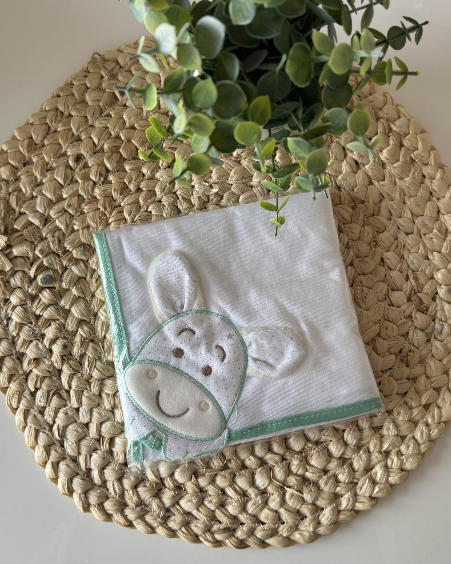 Toalha branca com aplicação de coelho cinzento sobre tapete de ráfia redondo