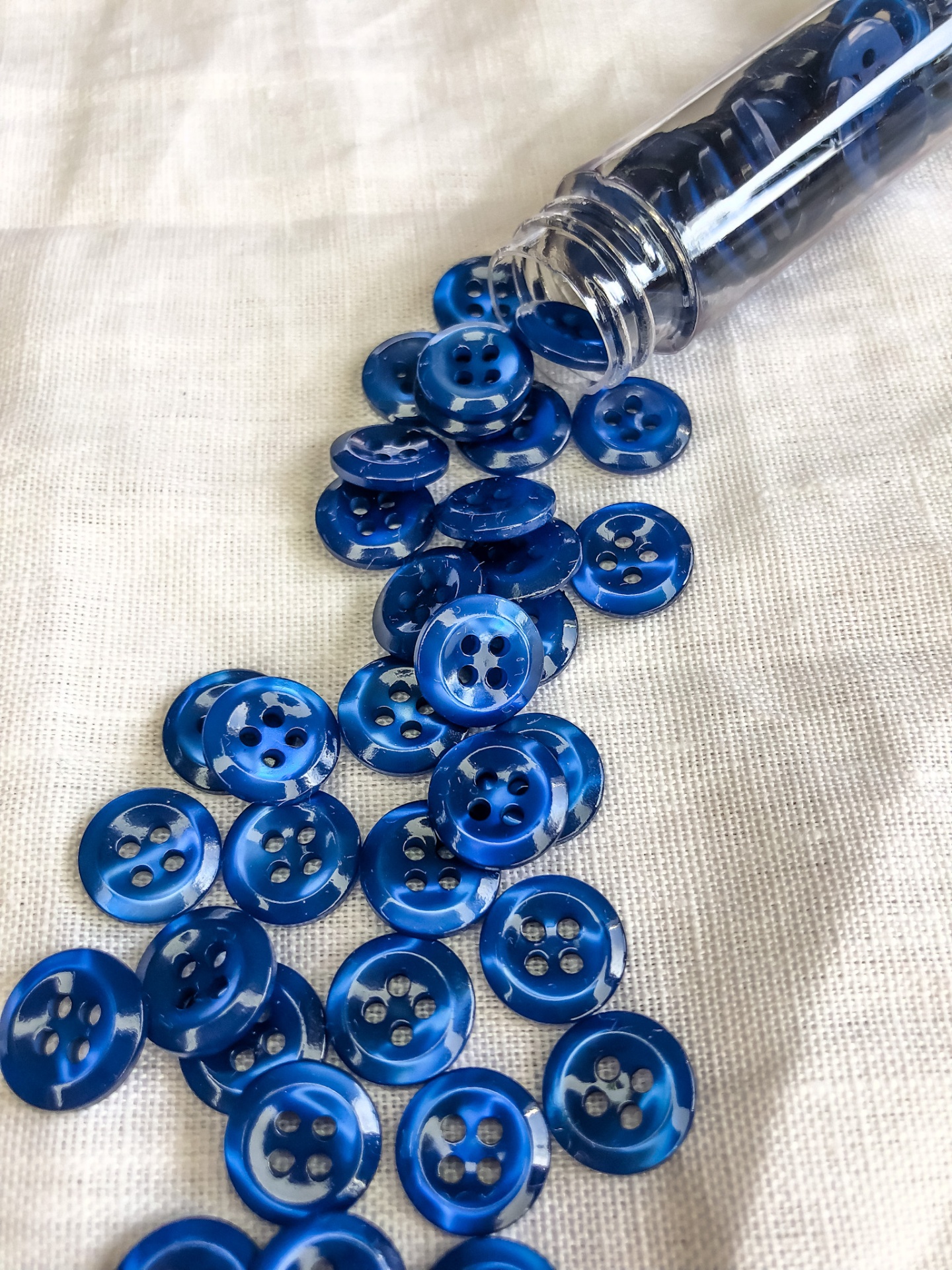 Botões redondos azuis de plástico com quatro furos sobre tecido branco.