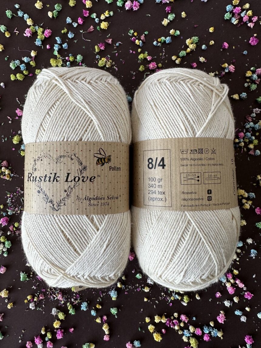 Novelos de fio de algodão cru Rustik Love com etiquetas castanhas sobre fundo escuro com flores coloridas