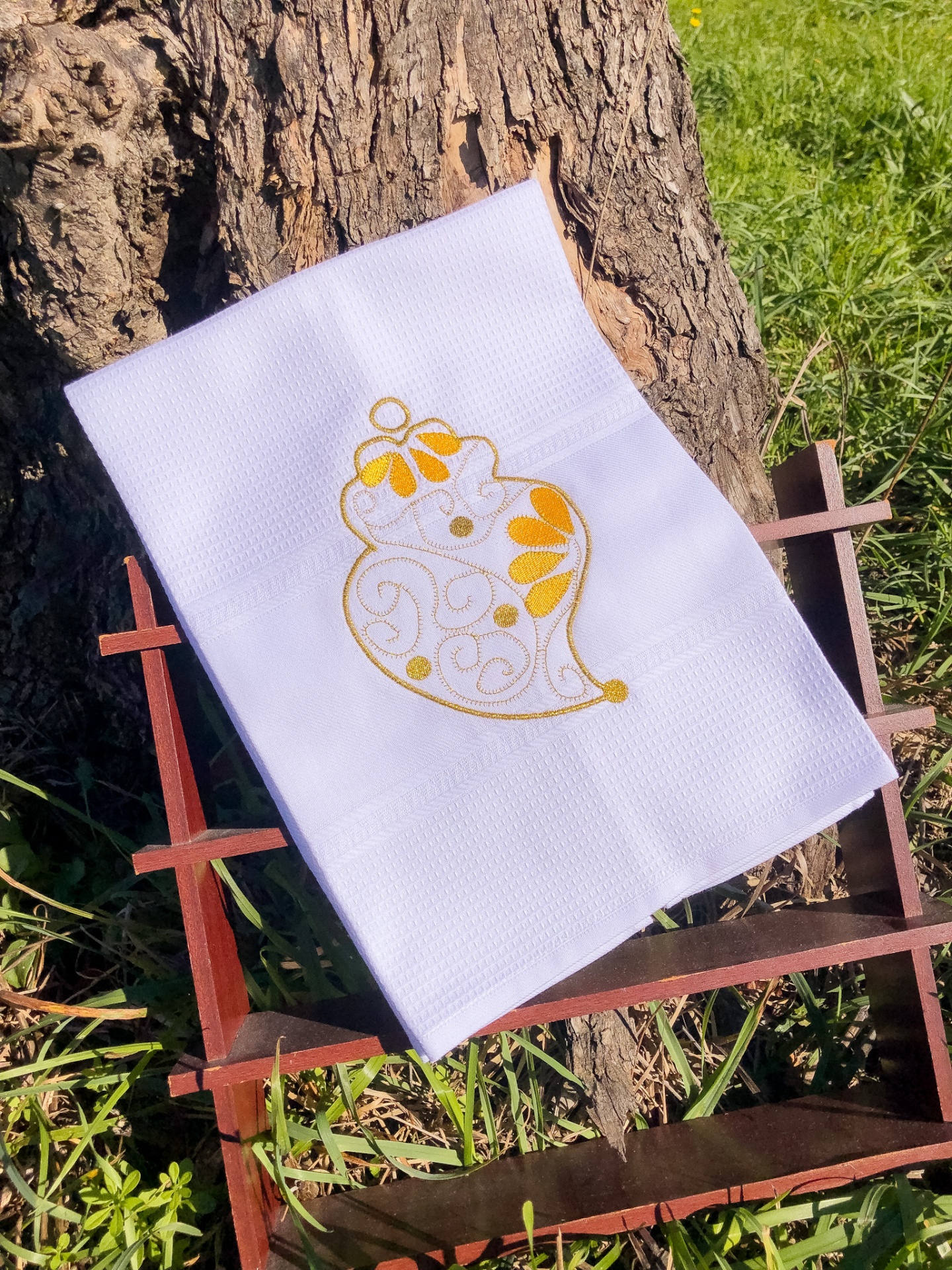 Toalha branca com bordado amarelo em suporte de madeira junto a uma árvore
